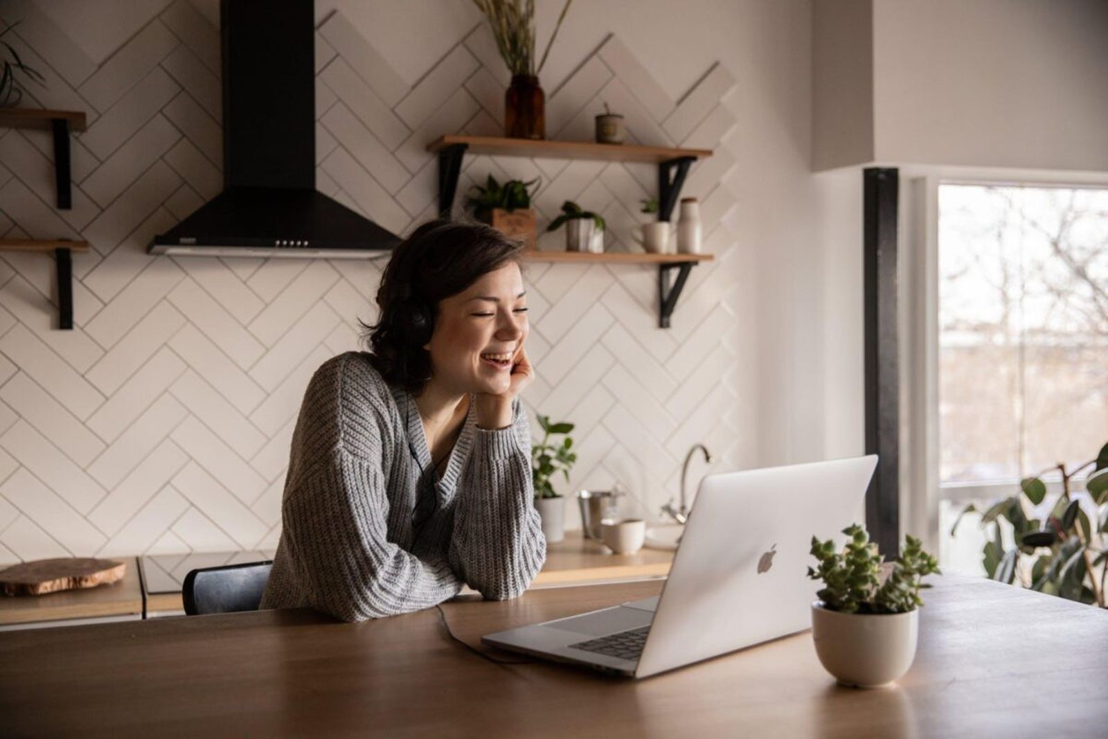 A woman smiling during a video call on her laptop at a kitchen table