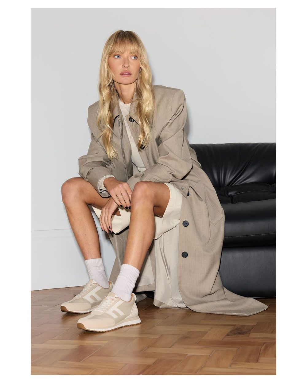 Woman sitting on a chair wearing beige sneakers and a trench coat