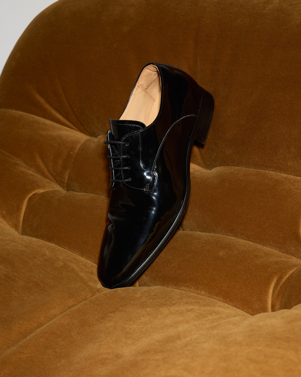 A single black patent leather dress shoe on an orange couch