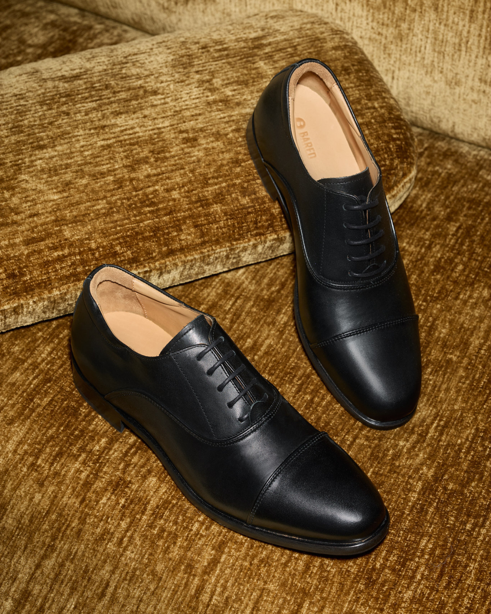 Pair of mens black leather dress shoes on a velvet couch