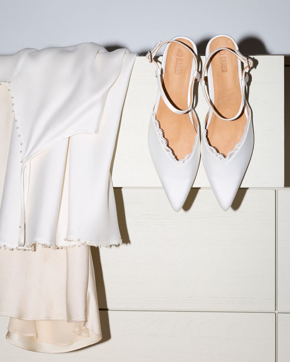 Whinchat white satin heels draped over a set of drawers