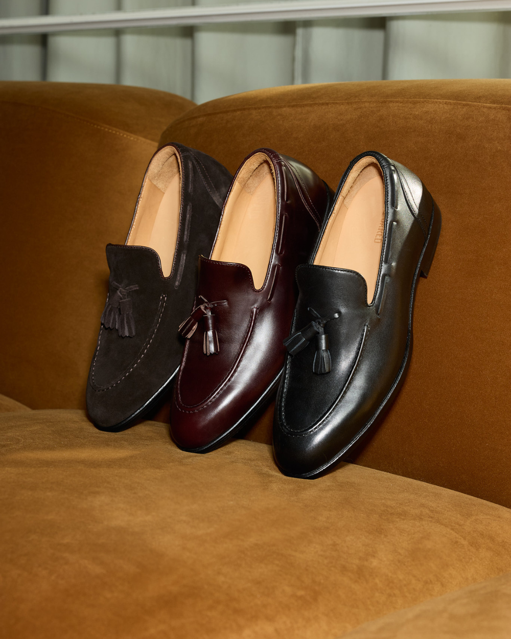 3 different coloured loafers with tassels lined up on a couch