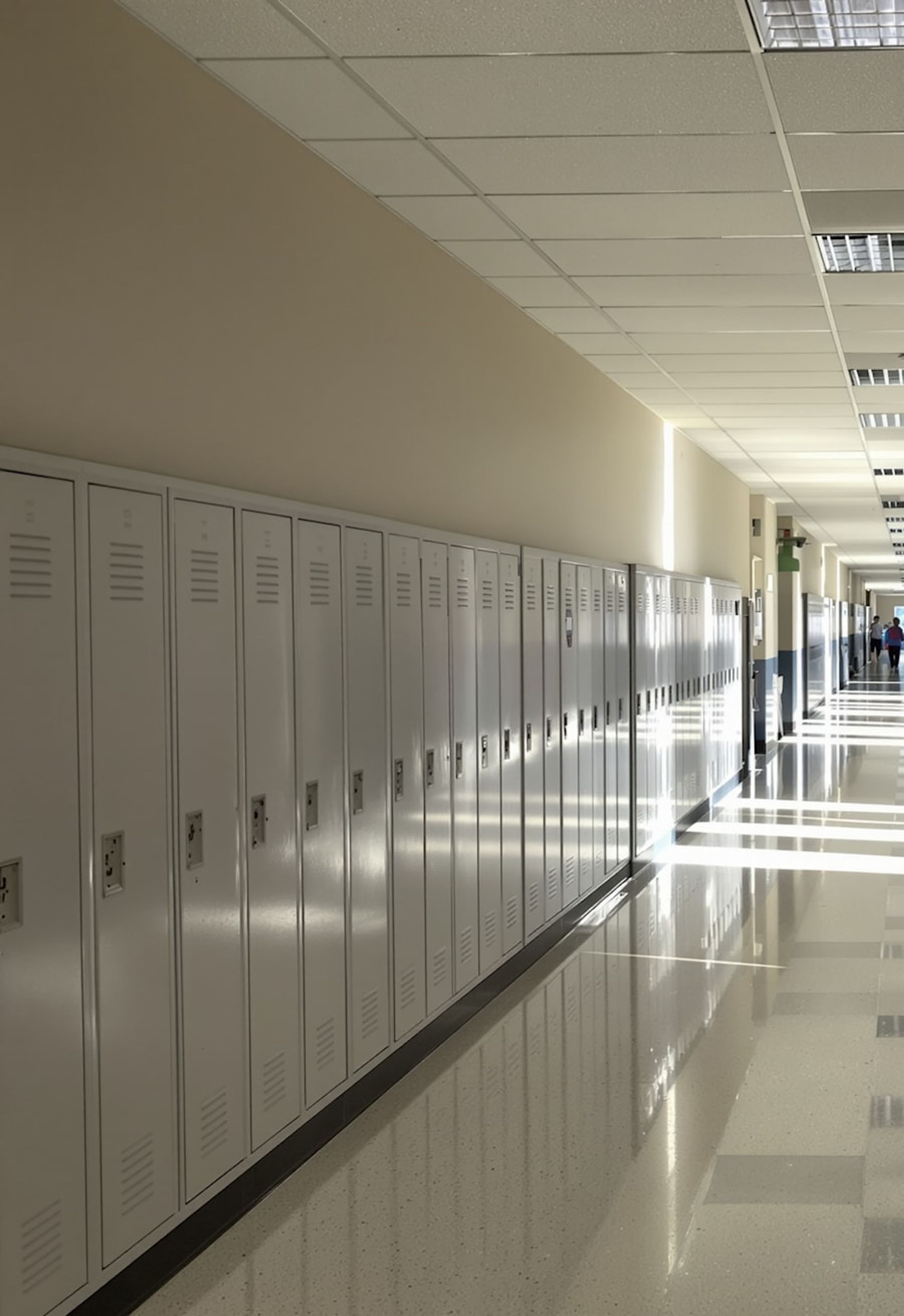 An empty school corridor lined with lockers, with sunlight falling across the floor.