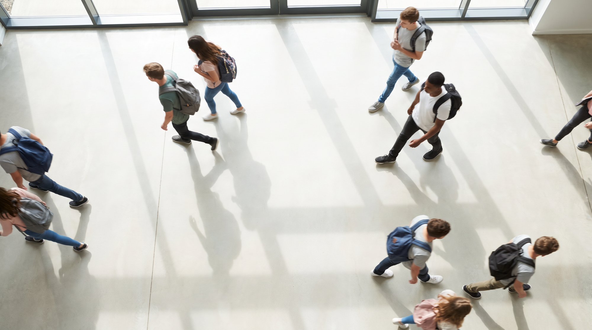 Students crossing a sunlit school atrium, seen from above.