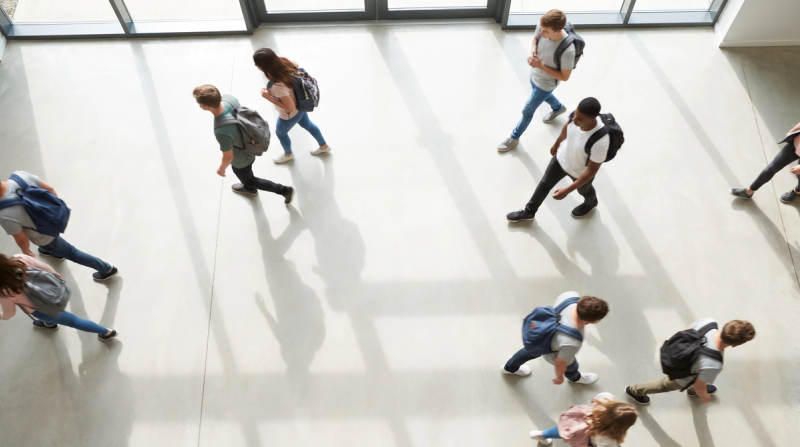 Students crossing a sunlit school atrium, seen from above.