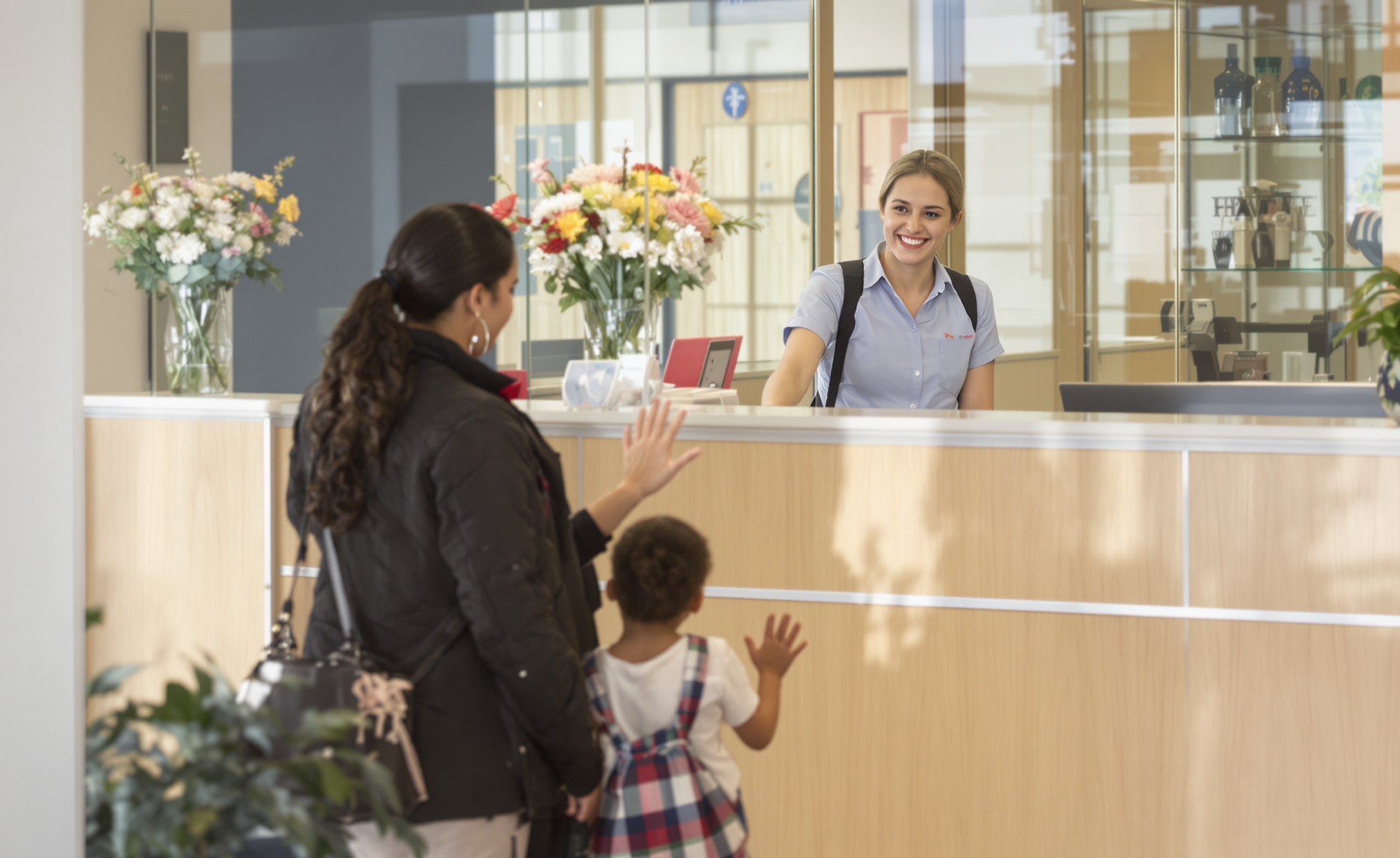 A smiling front office staff member greeting a parent and child at a school welcome desk