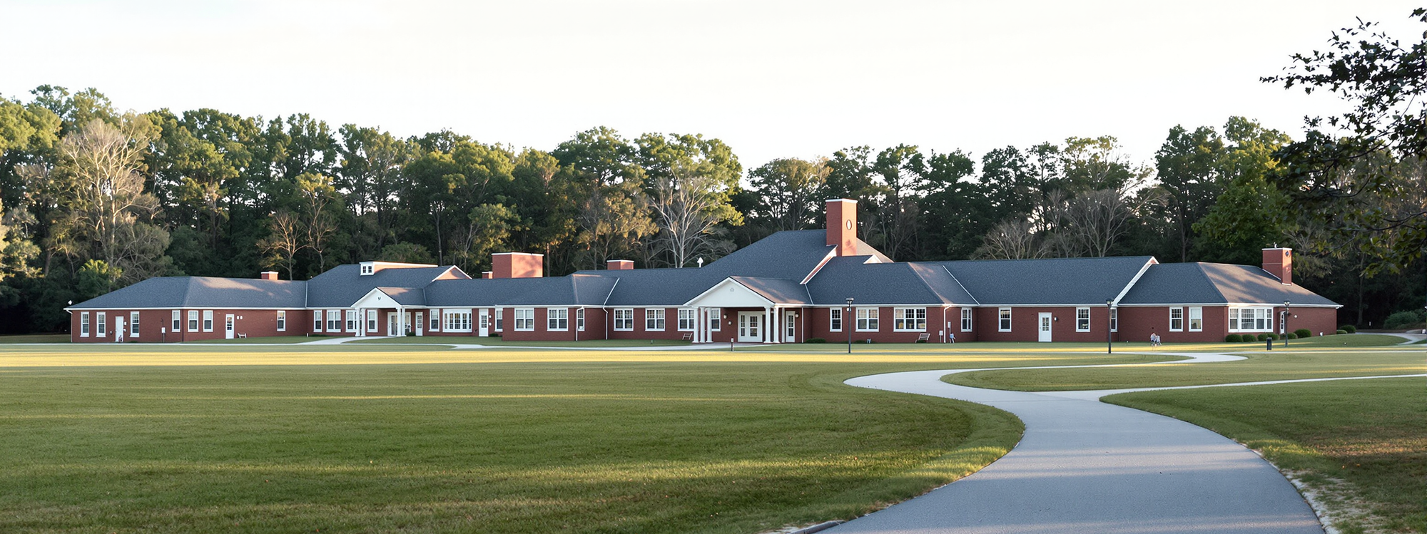 A low brick school building set back behind a lawn and mature trees