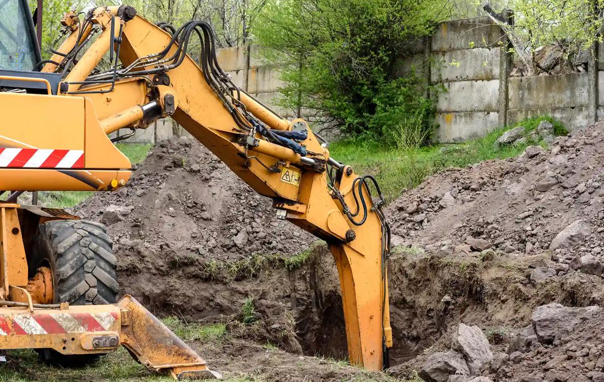 Excavator digging a trench with piles of excavated soil and spoil ready for removal in Sydney