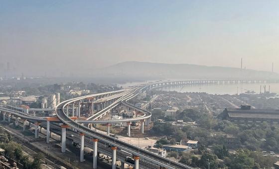 An aerial view of the multi-lane Sewri interchange of the Atal Setu bridge curving over the coastline and urban landscape in Mumbai during a hazy day.