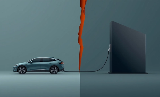 A minimalist illustration on a light ash background showing a teal geometric car shape connected to a dark obsidian charging monolith by a thick grey cable that is sharply severed in the centre.