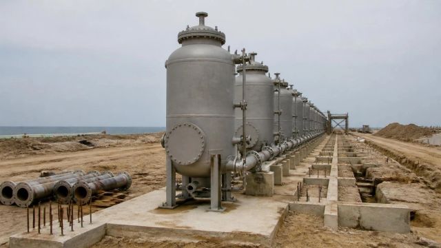 Unfinished water treatment vessels in a row on a construction site, with pipework running toward the horizon.