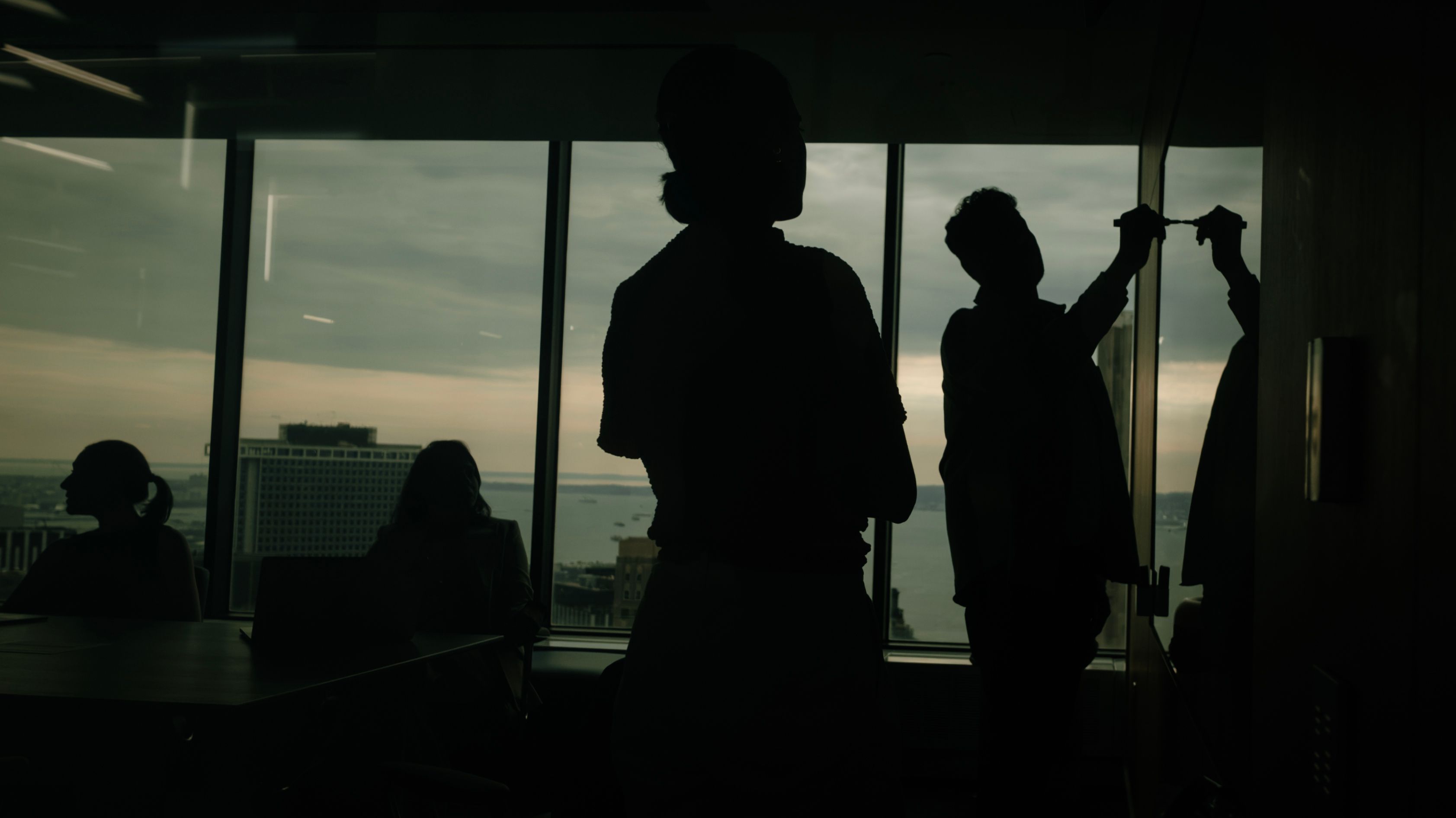 Silhouetted team members working by floor-to-ceiling windows overlooking the harbour