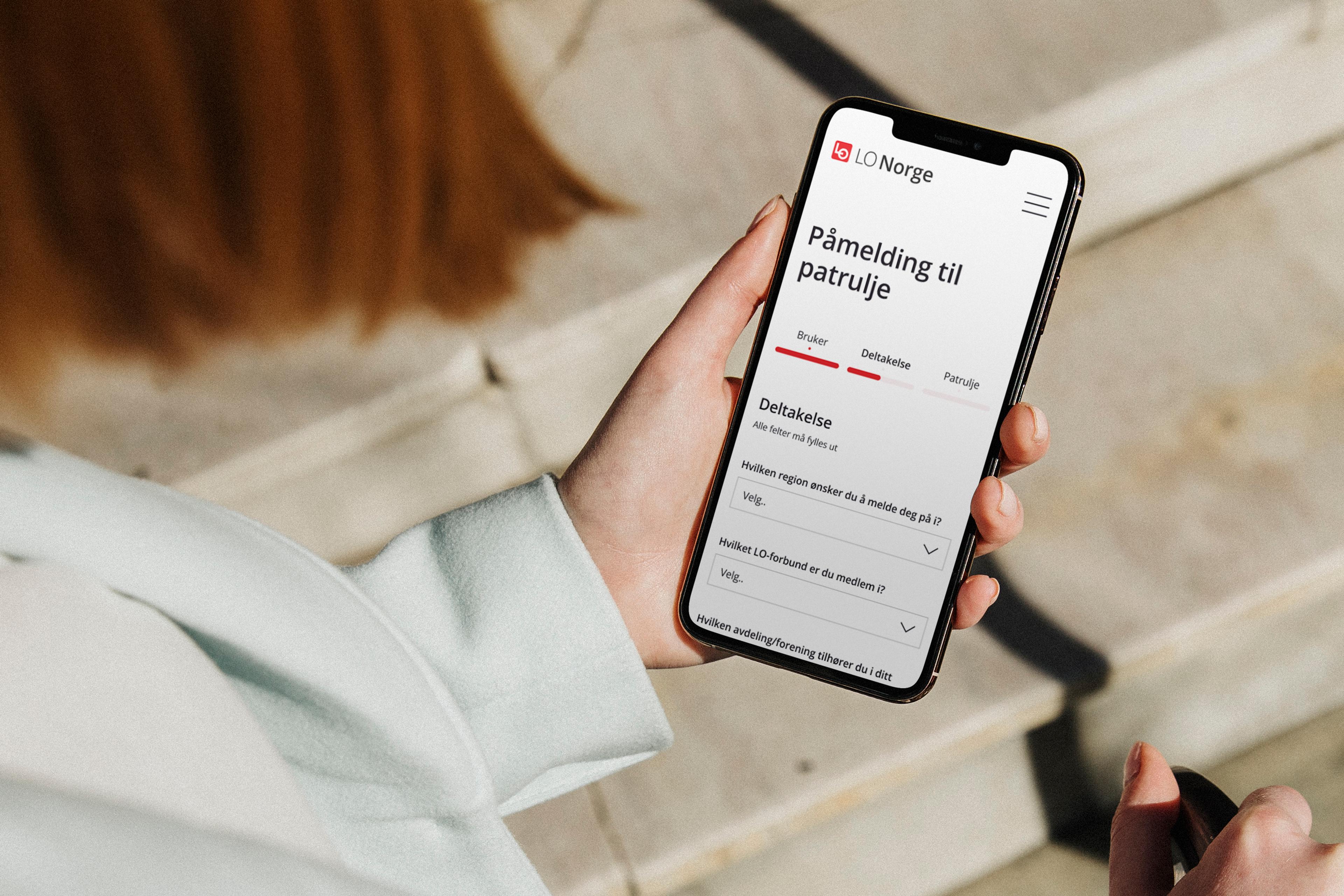 Hånd holder smarttelefon utendørs. Skjerm viser påmeldingsskjema.
