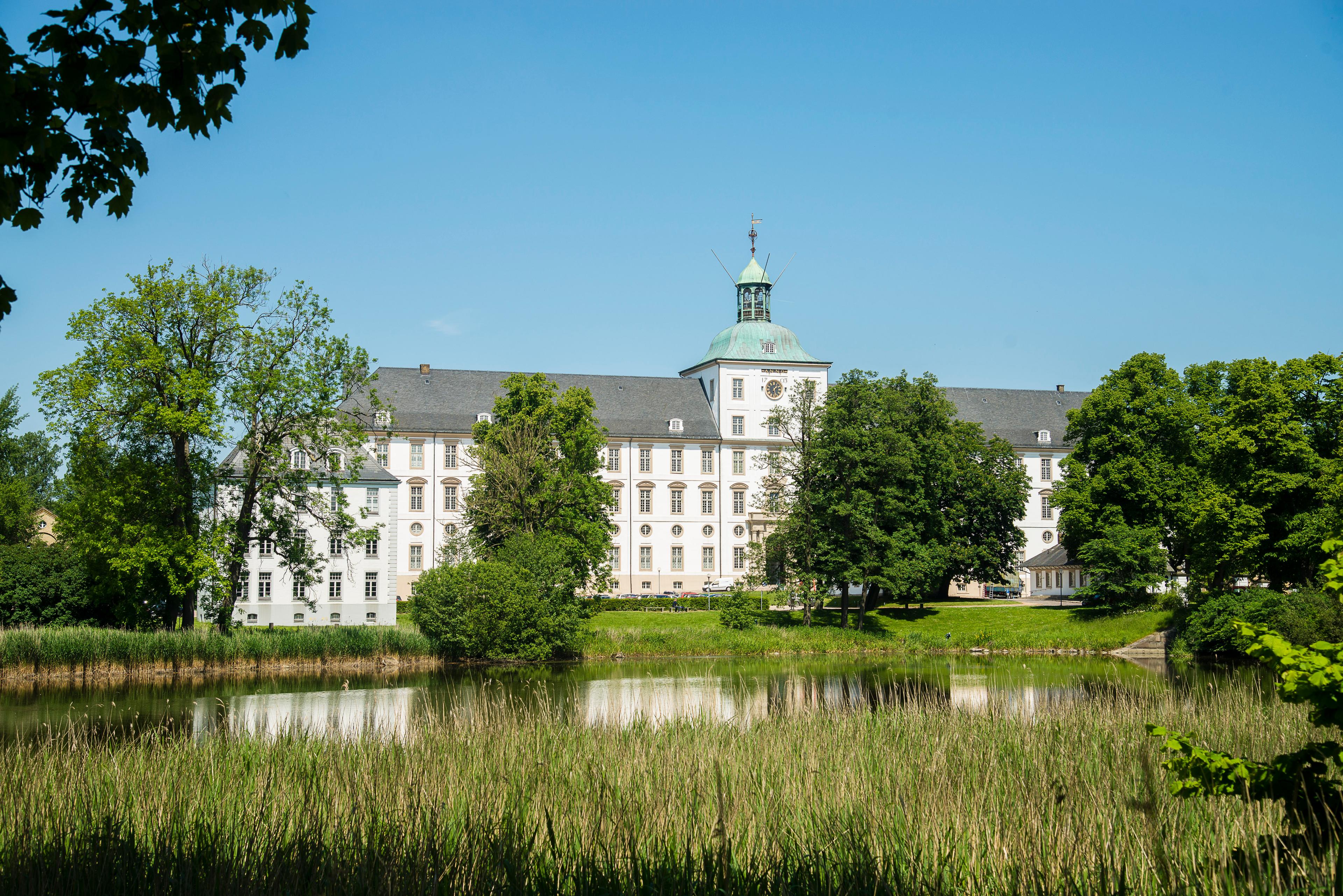 Ein großes, historisches Schloss mit einem Park und einem Teich im Vordergrund