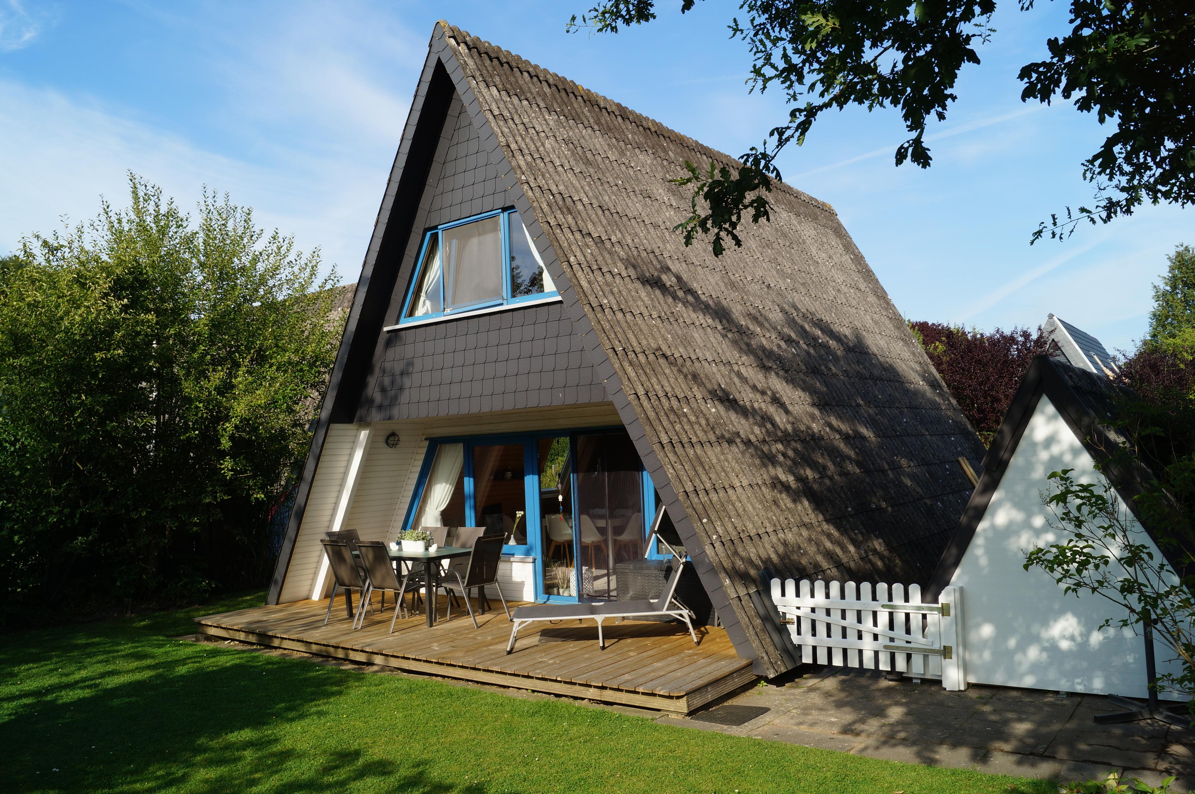 Ein A-Frame Haus mit einer Holzterrasse, umgeben von Bäumen und einem gepflegten Rasen
