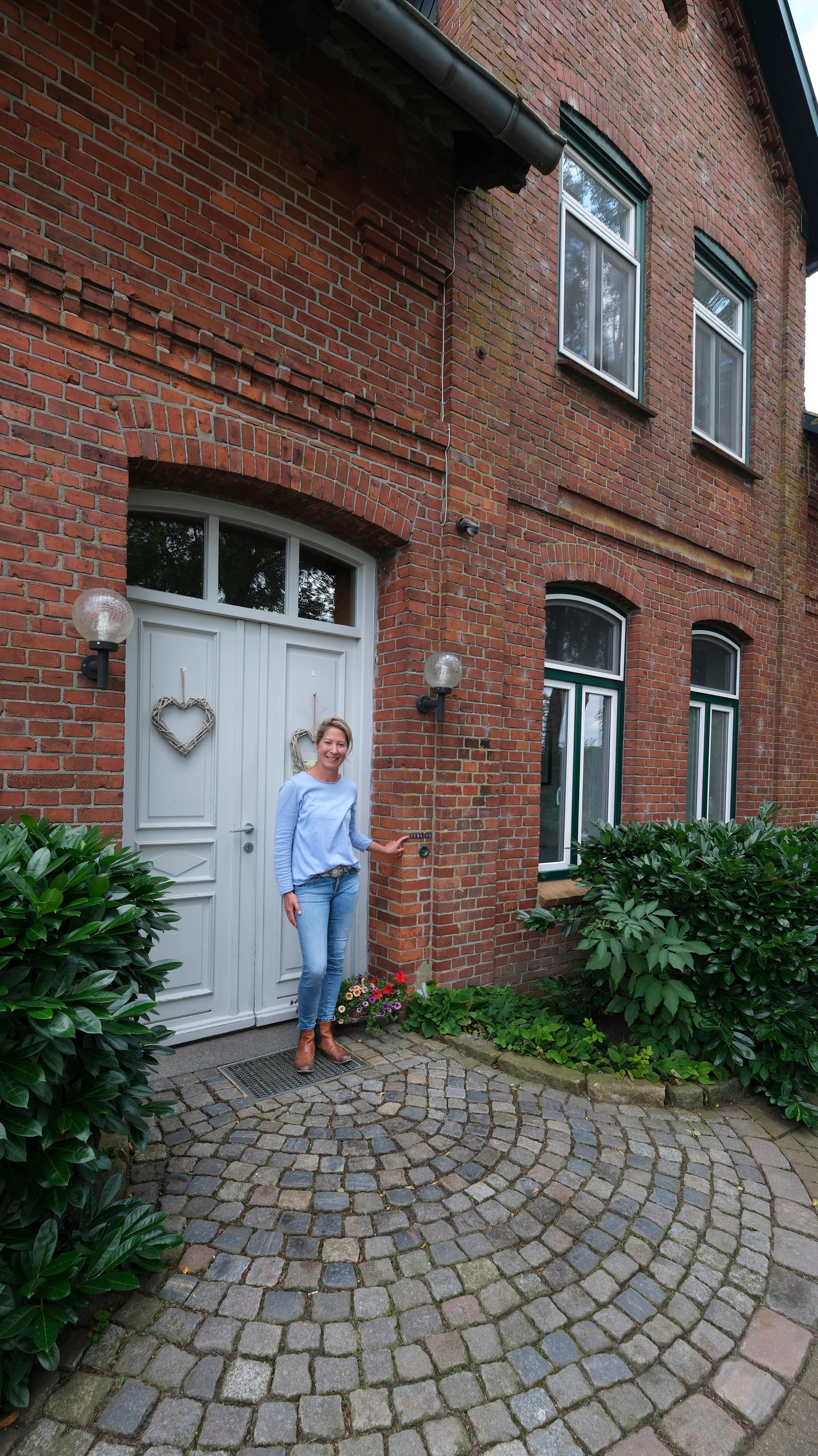 Eine Frau steht vor einem traditionellen Backsteinhaus mit einer weißen Tür und Herzdekorationen