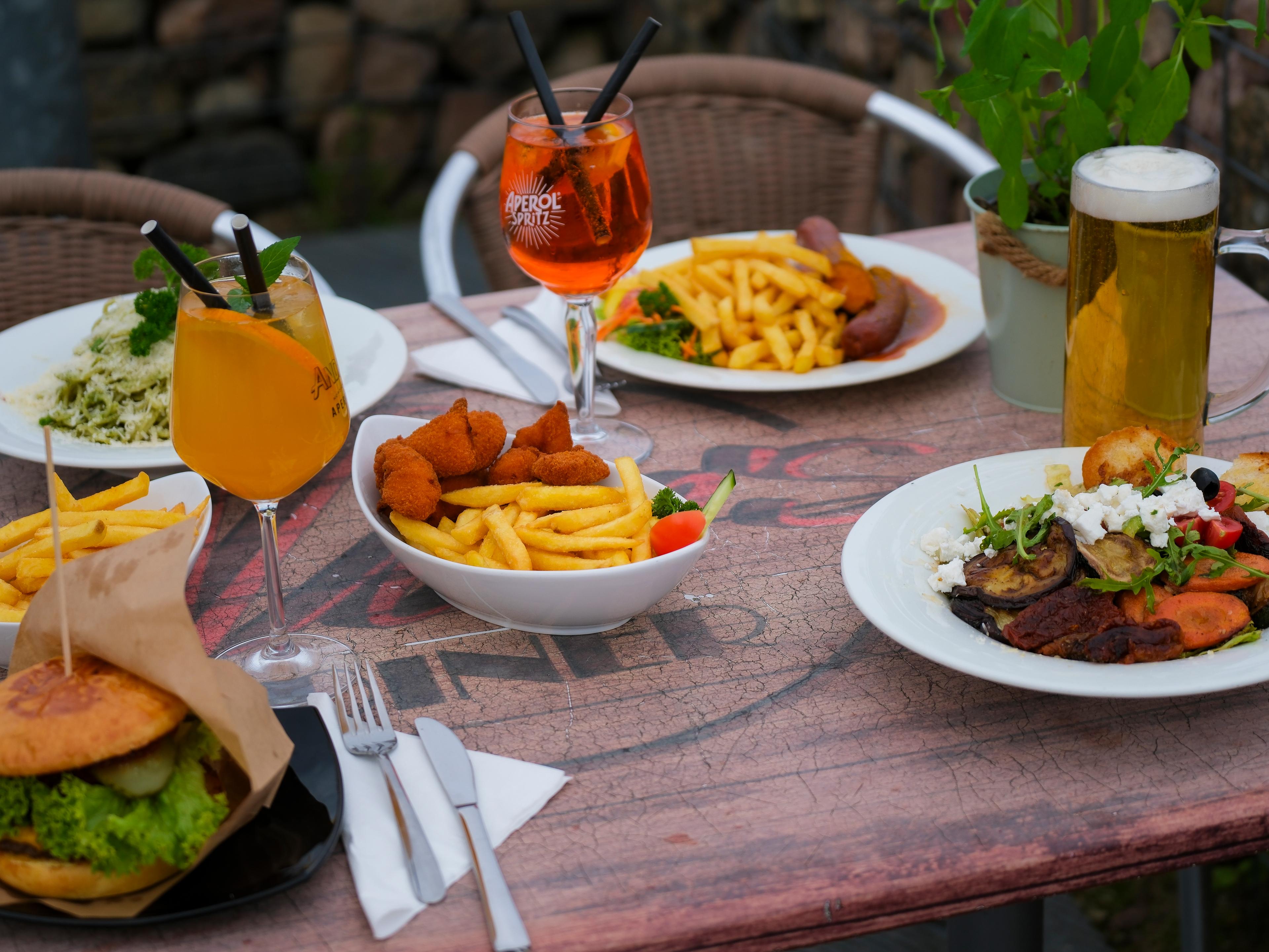 Ein Tisch im Freien mit verschiedenen Gerichten, darunter ein Burger, Pommes, Salat und Getränke