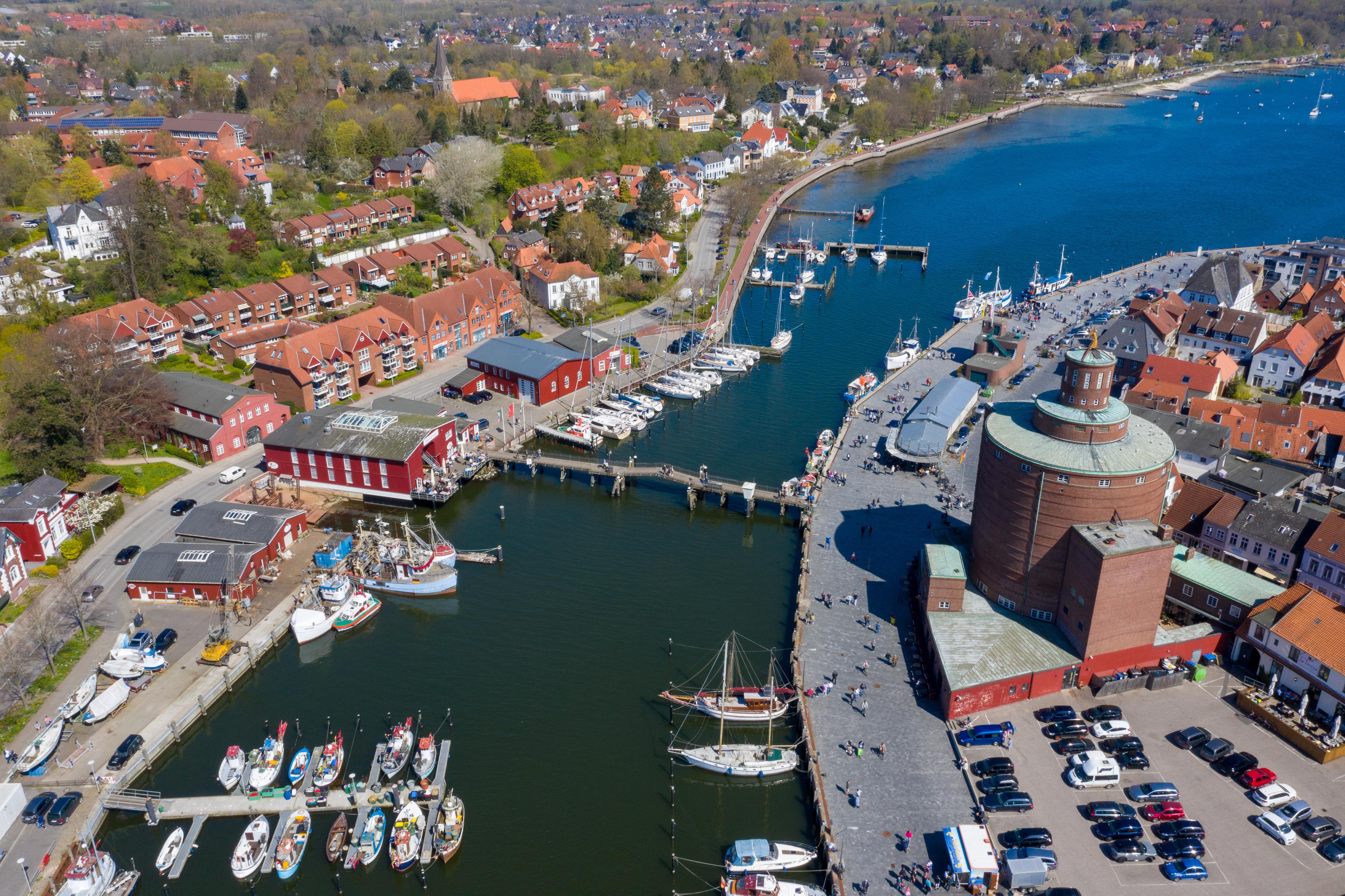 Luftaufnahme einer Hafenstadt mit Yachthafen, roten Gebäuden und einem runden Turm