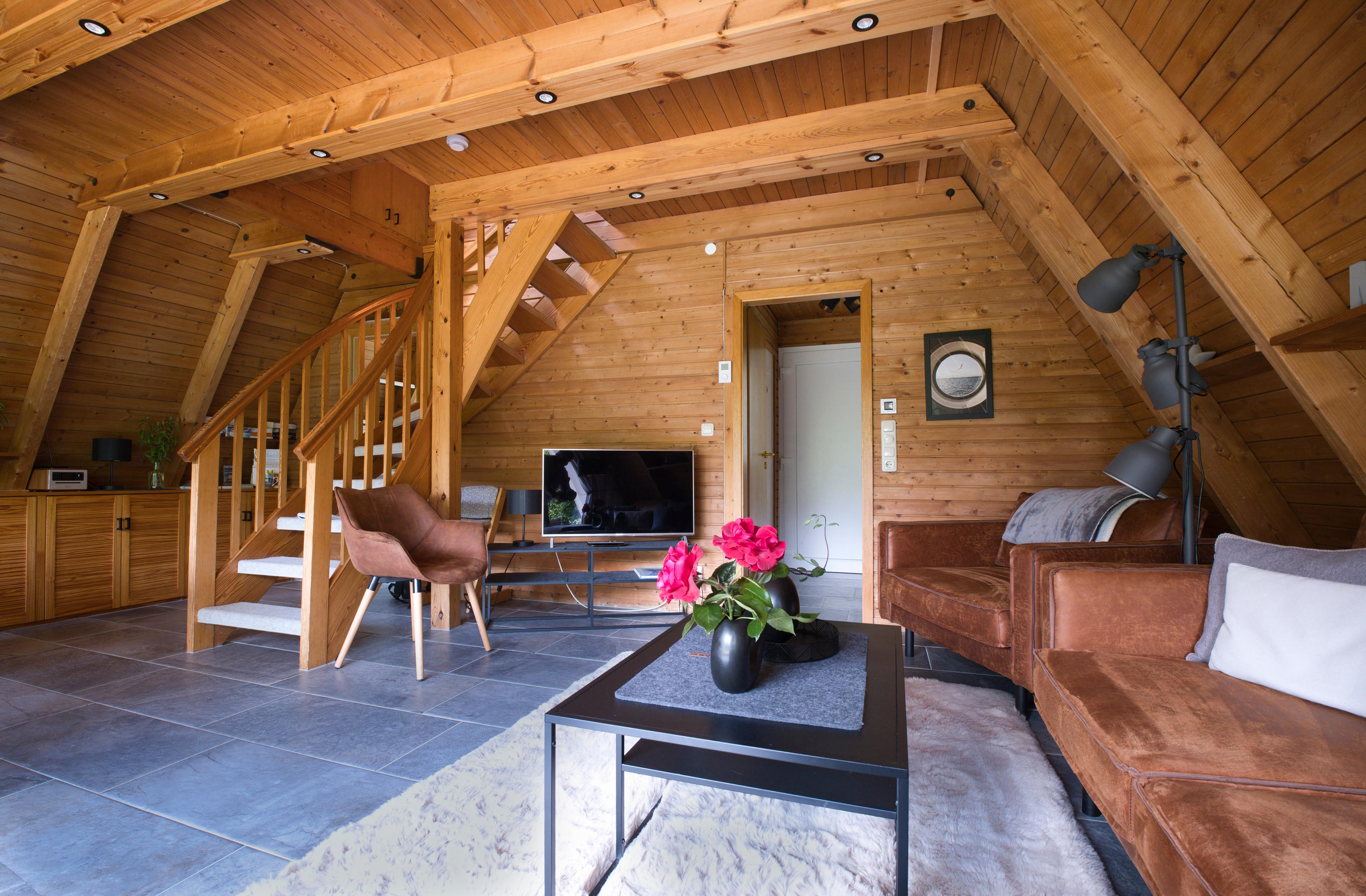 Ein gemütliches Wohnzimmer mit Holzdecke, Ledersofa, Fernseher und Treppe