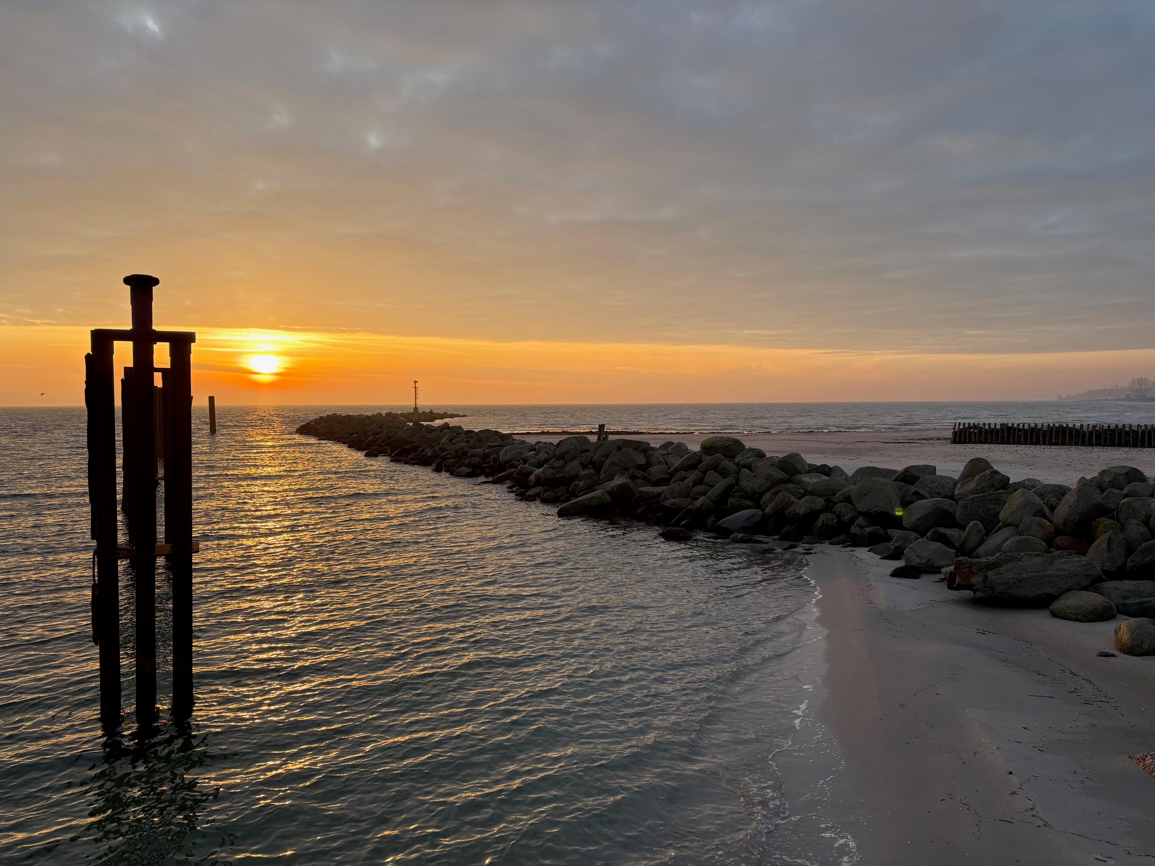 Ein Sandstrand mit einer Steinmole und einem ruhigen Meer bei Sonnenuntergang