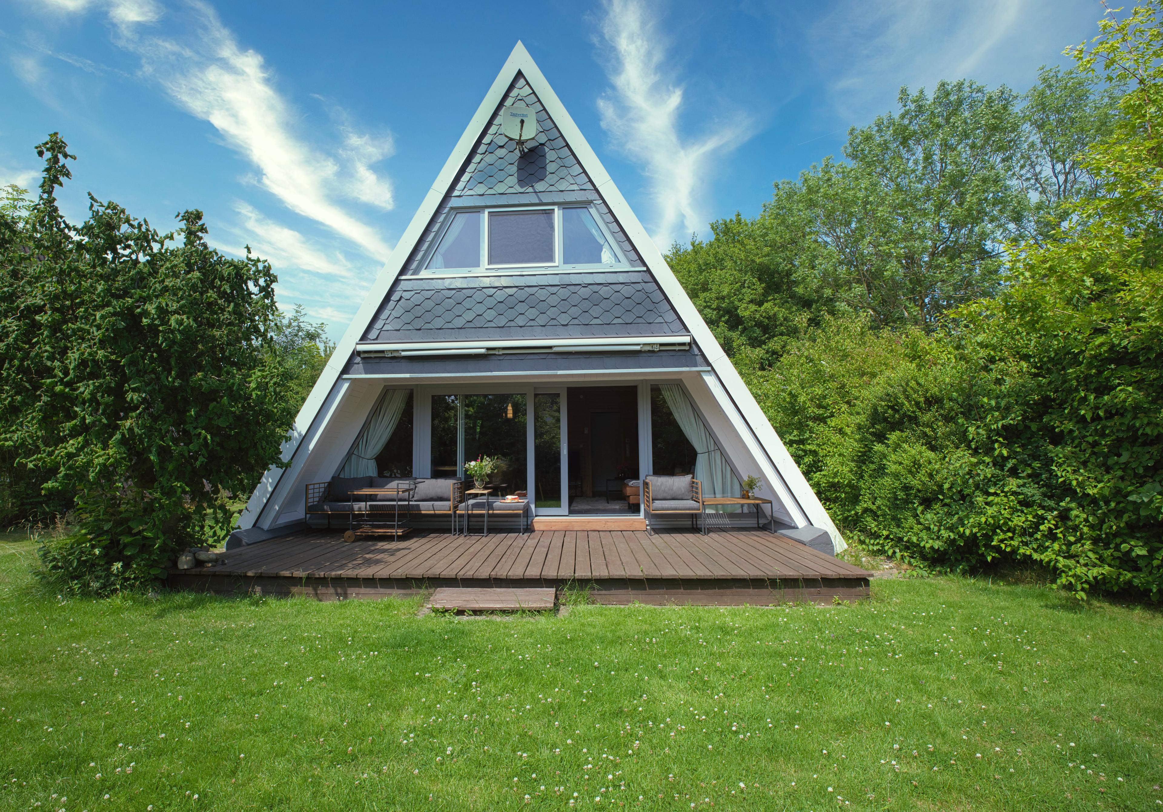 Ein modernes A-Frame Haus mit einer Holzterrasse, umgeben von üppigem Grün und blauem Himmel