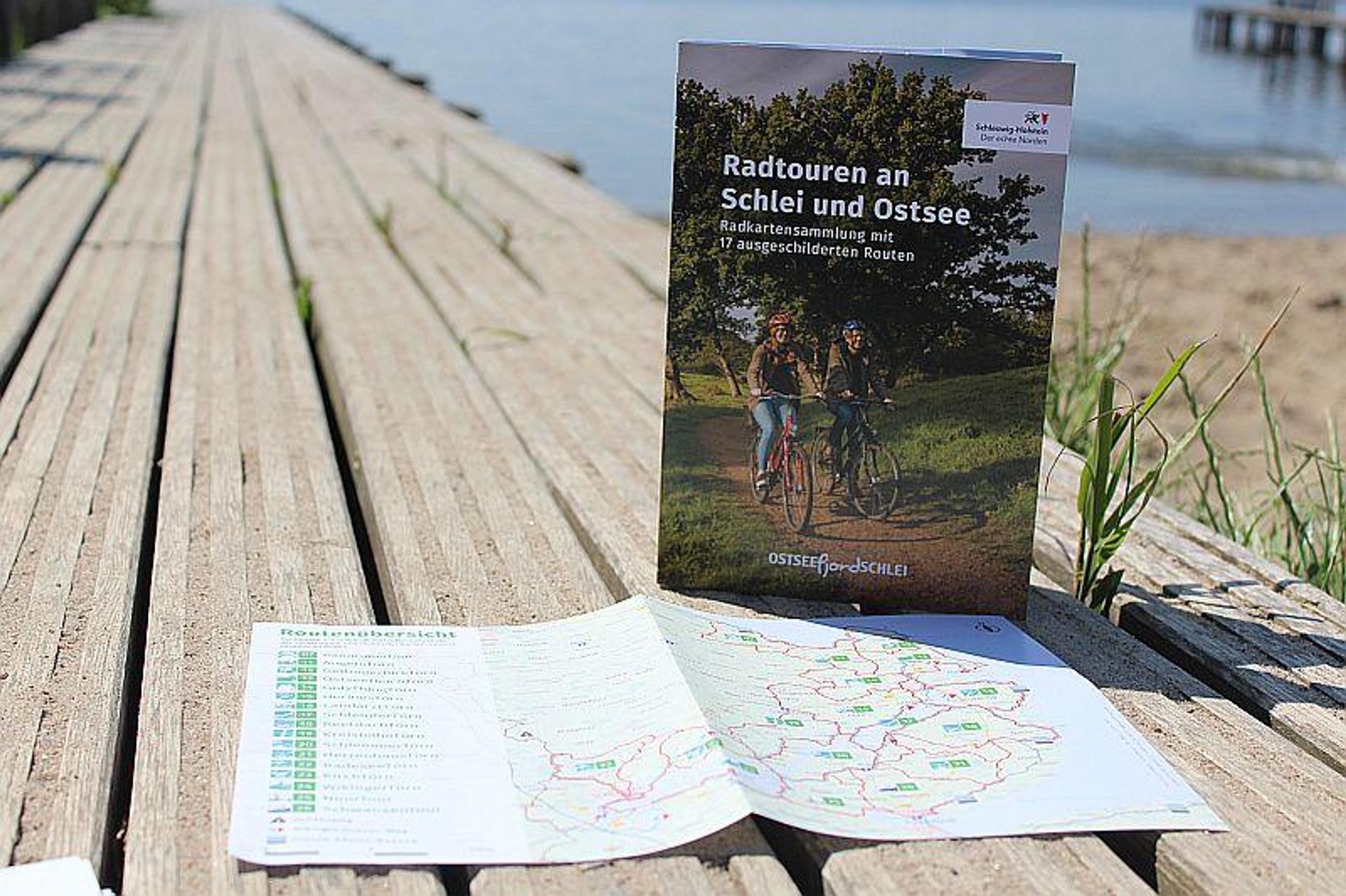 Broschüre über Radtouren an Schlei und Ostsee auf einem Holzsteg am Strand mit einer Karte