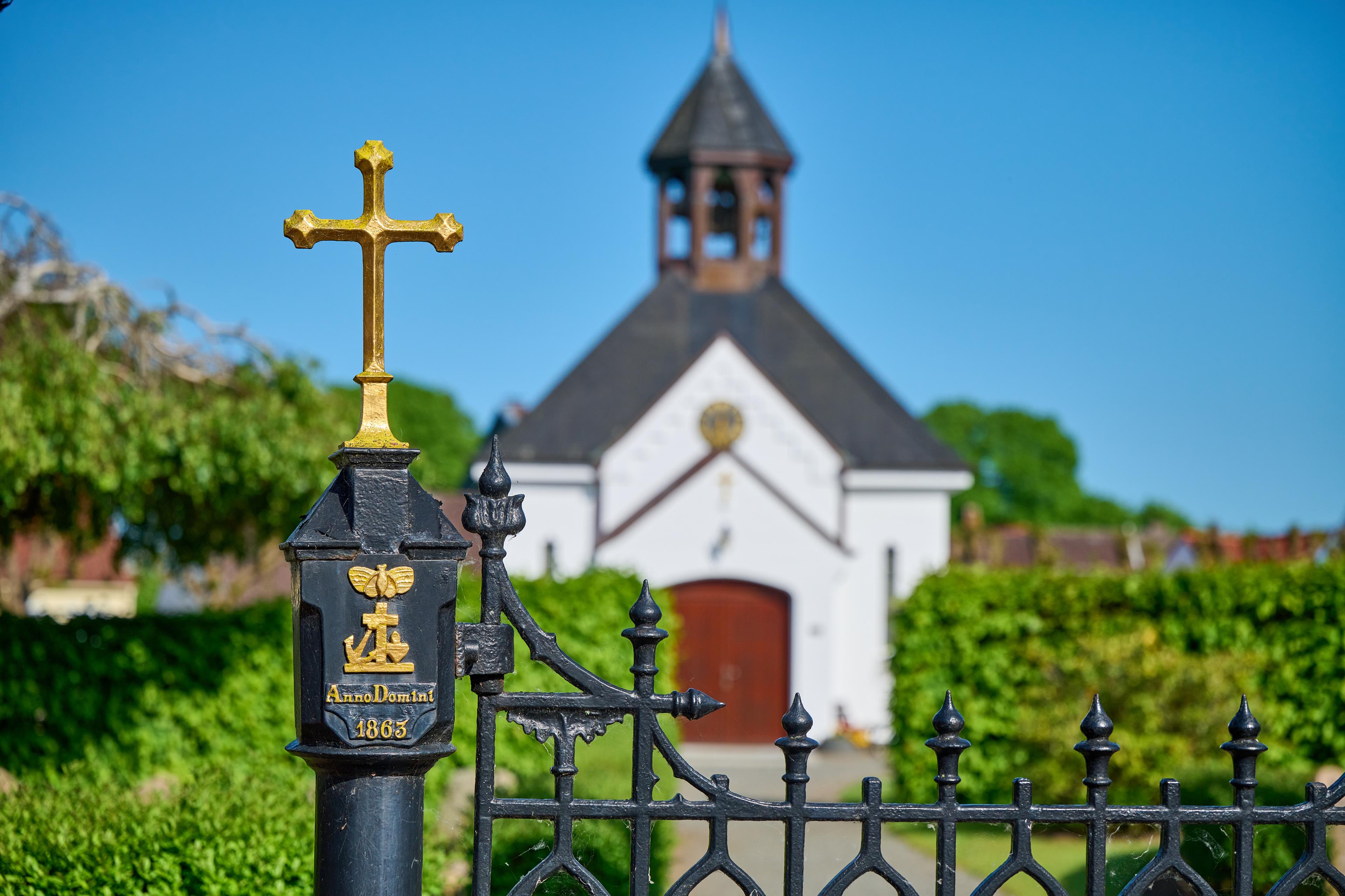 Ein dekoratives Eisengitter mit einem goldenen Kreuz im Vordergrund und eine historische Kirche im Hintergrund