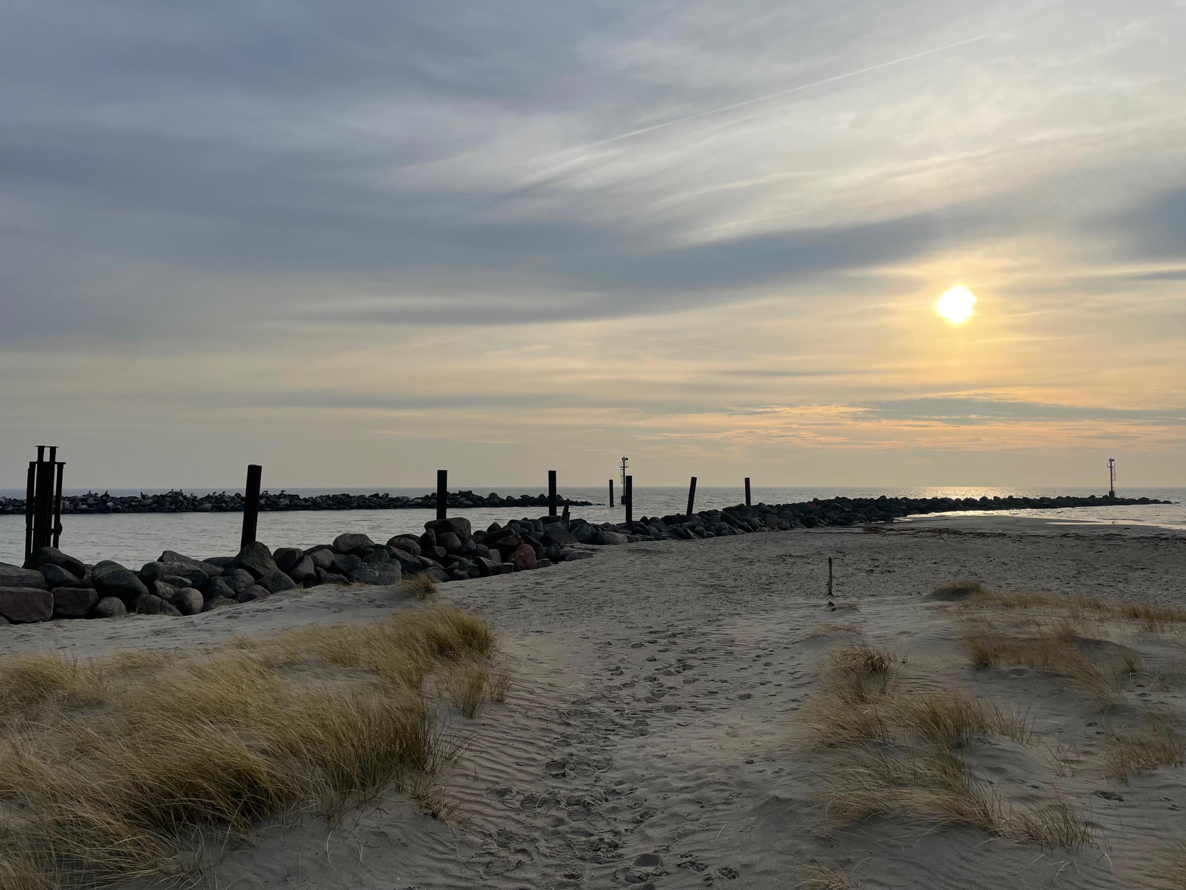 Ein Sandstrand mit einer Steinmole und einem ruhigen Meer bei Sonnenuntergang