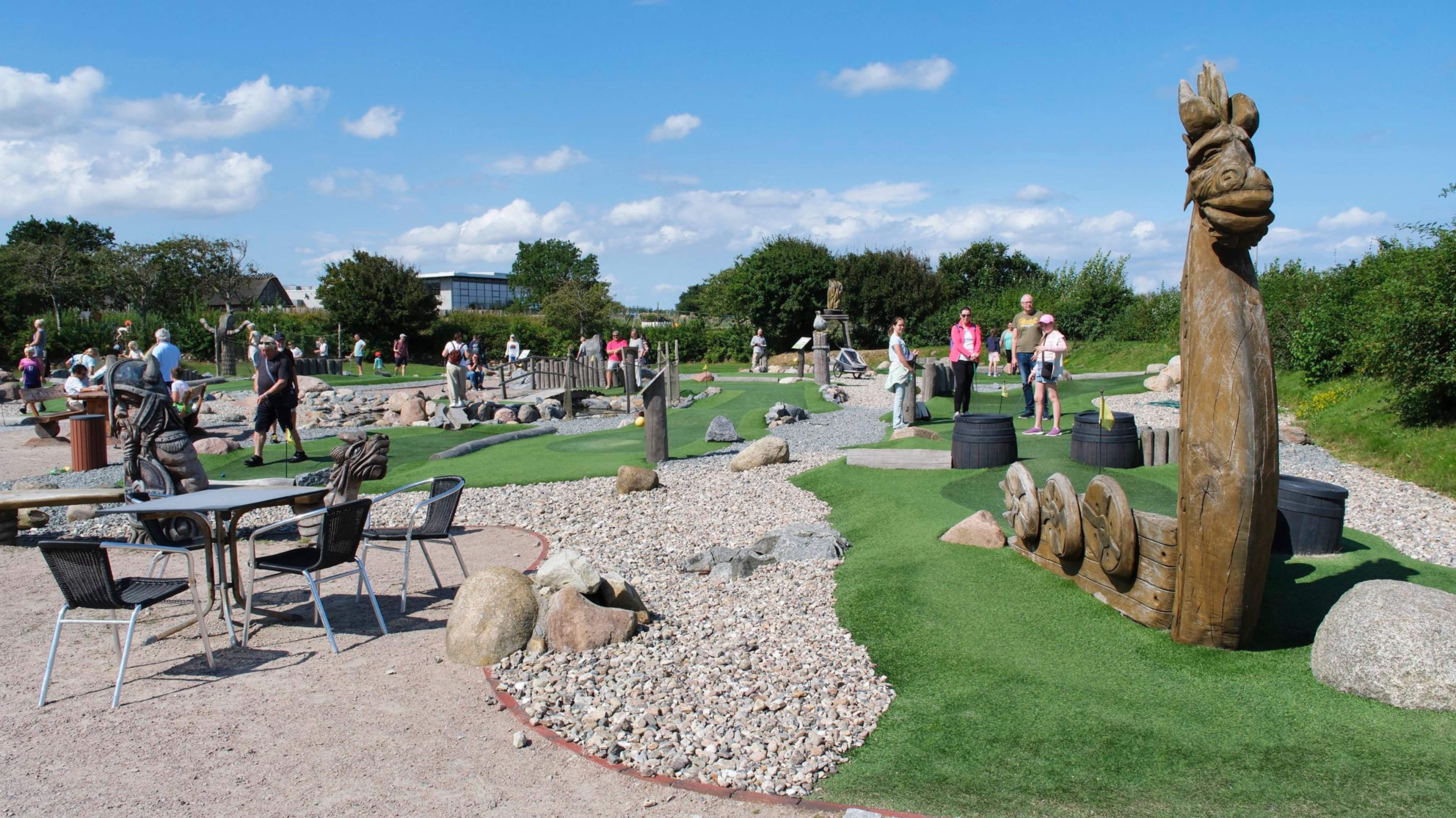 Ein Outdoor-Minigolfplatz mit Holzskulpturen und mehreren Spielern bei sonnigem Wetter