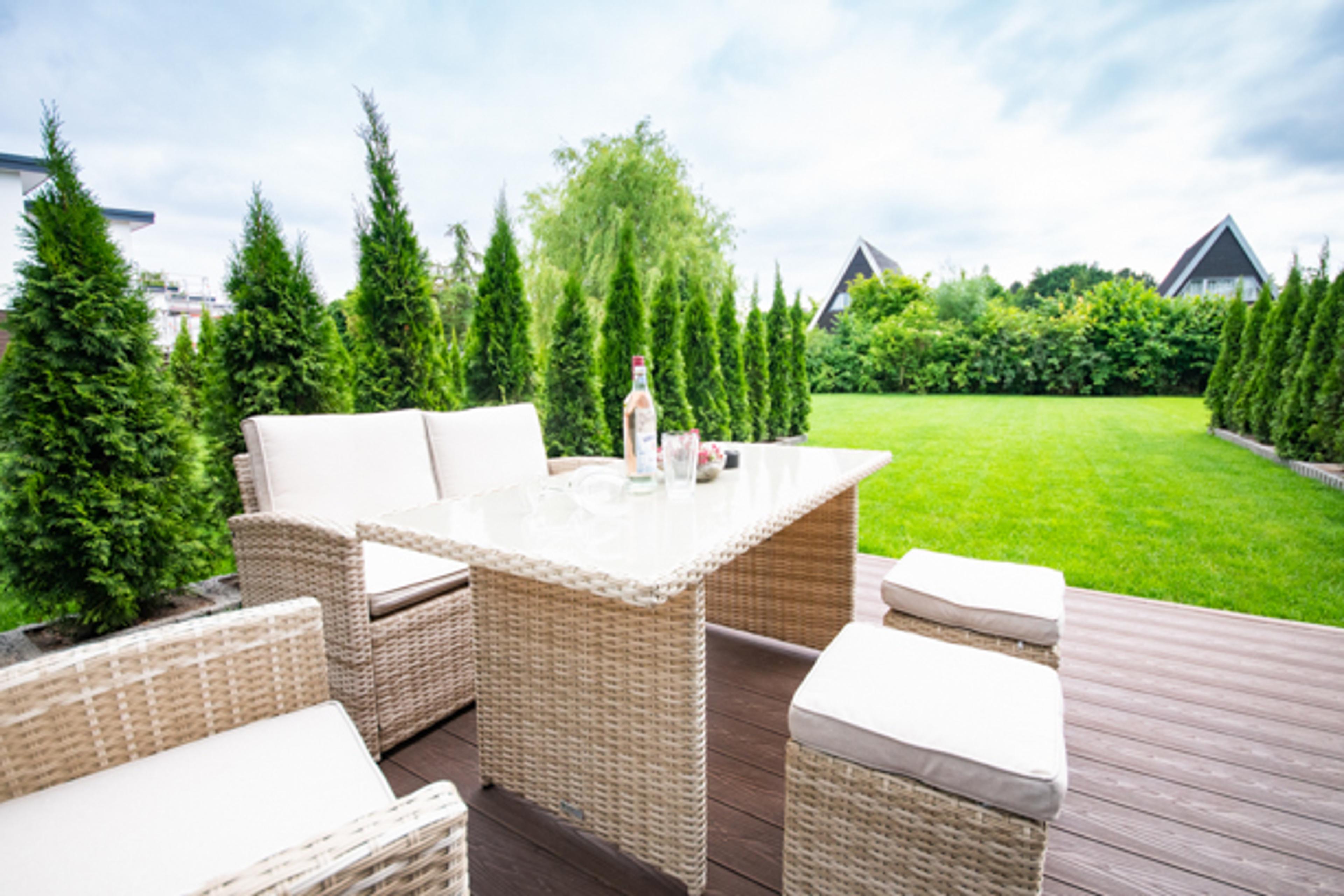 Eine moderne Terrasse mit Rattanmöbeln, einem Tisch mit Getränken und Blick auf einen gepflegten Garten