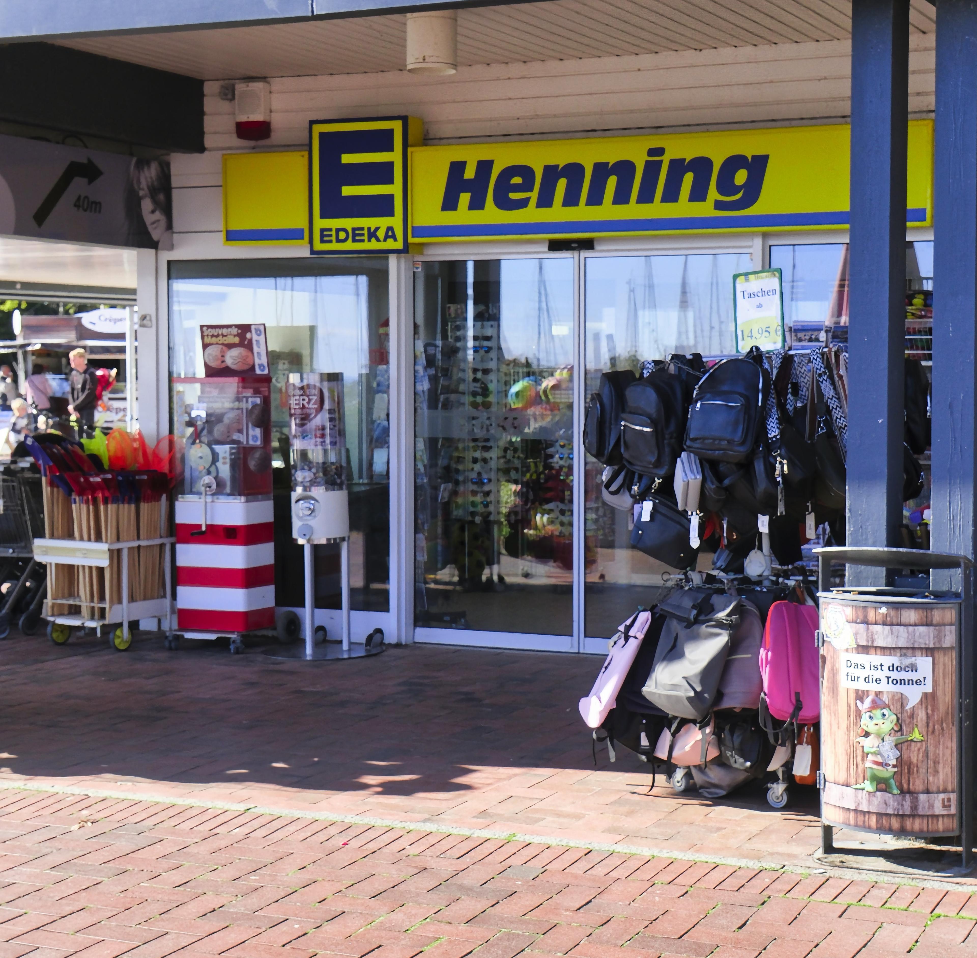 Edeka Henning-Ladenfront mit einer Auslage von Rucksäcken und verschiedenen Artikeln im Außenbereich.