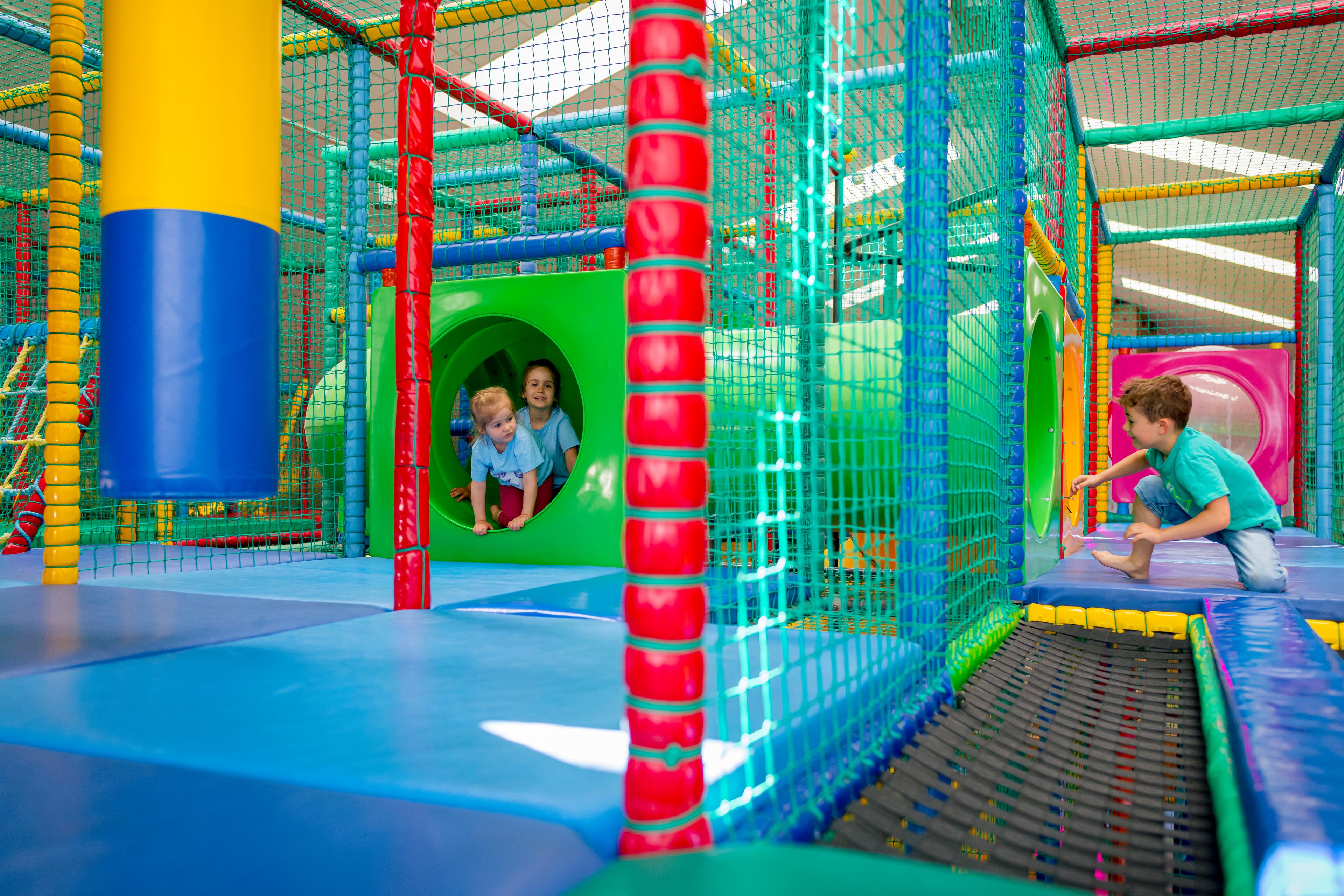 Kinder spielen in einem bunten Indoor-Spielplatz mit Klettergerüst und Rutsche