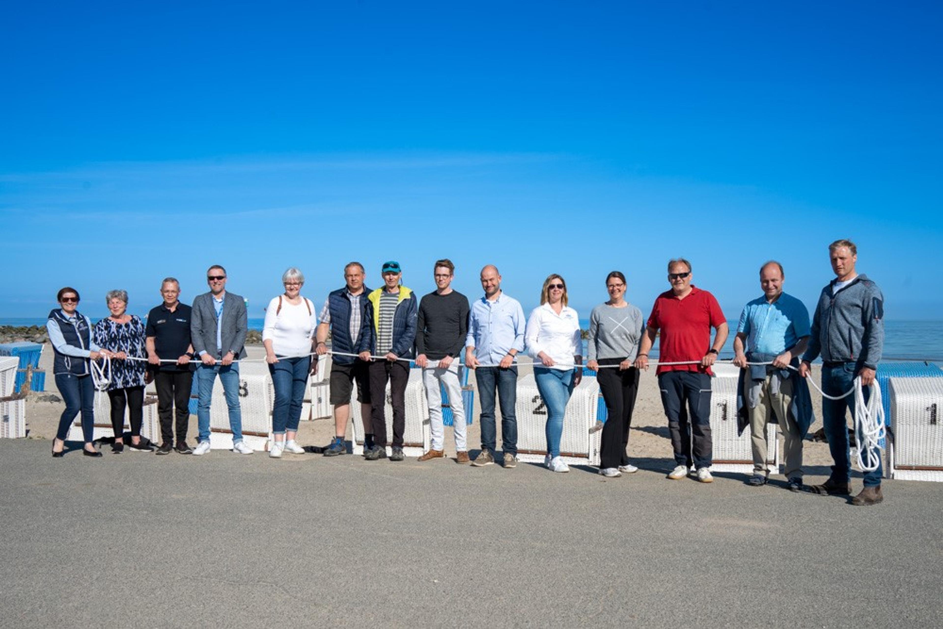 Eine Gruppe von Vereinsmitglieder steht am Strand und hält ein langes Seil vor sich.