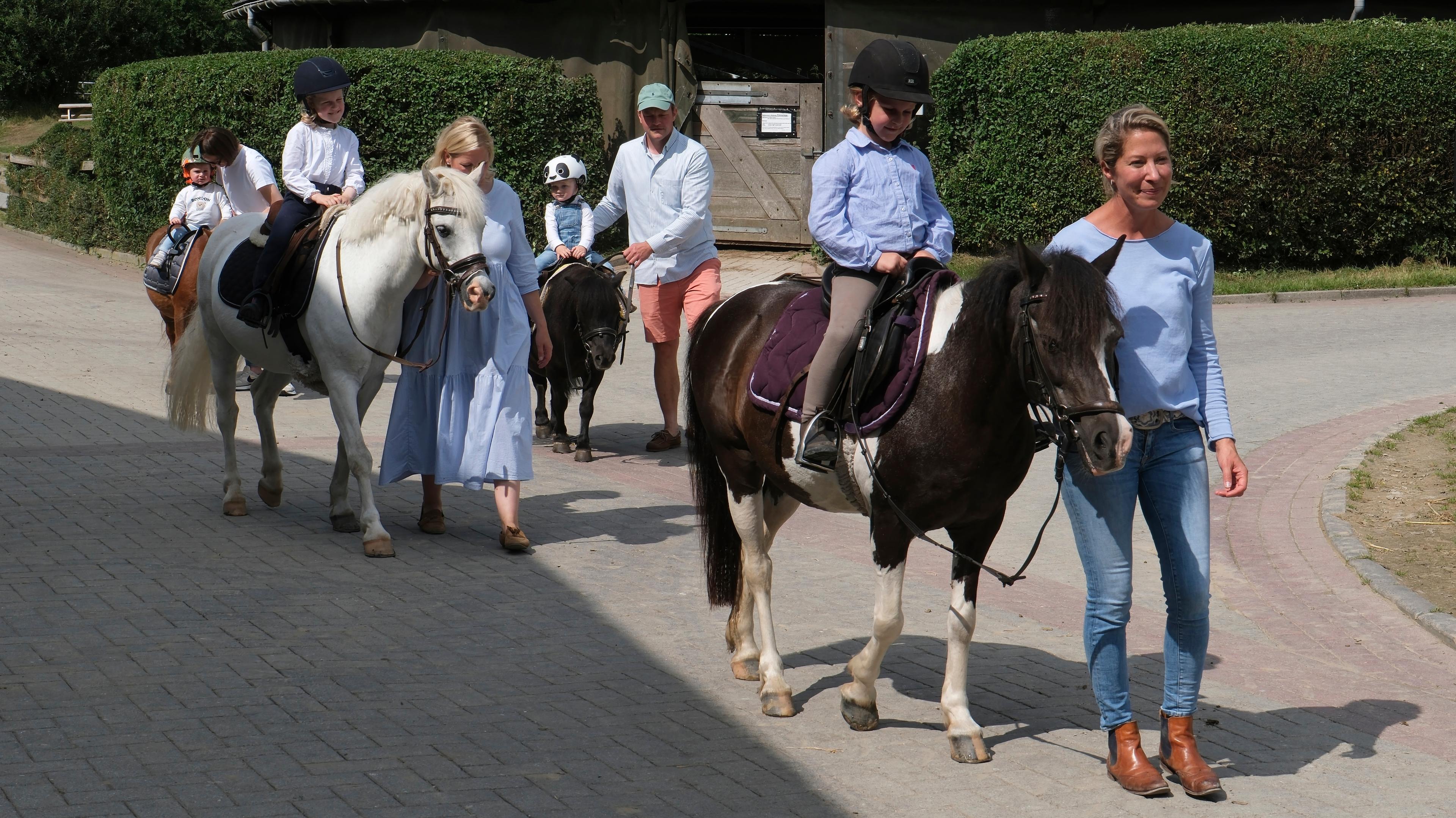 Kinder reiten auf Ponys, begleitet von Erwachsenen auf einem Hof