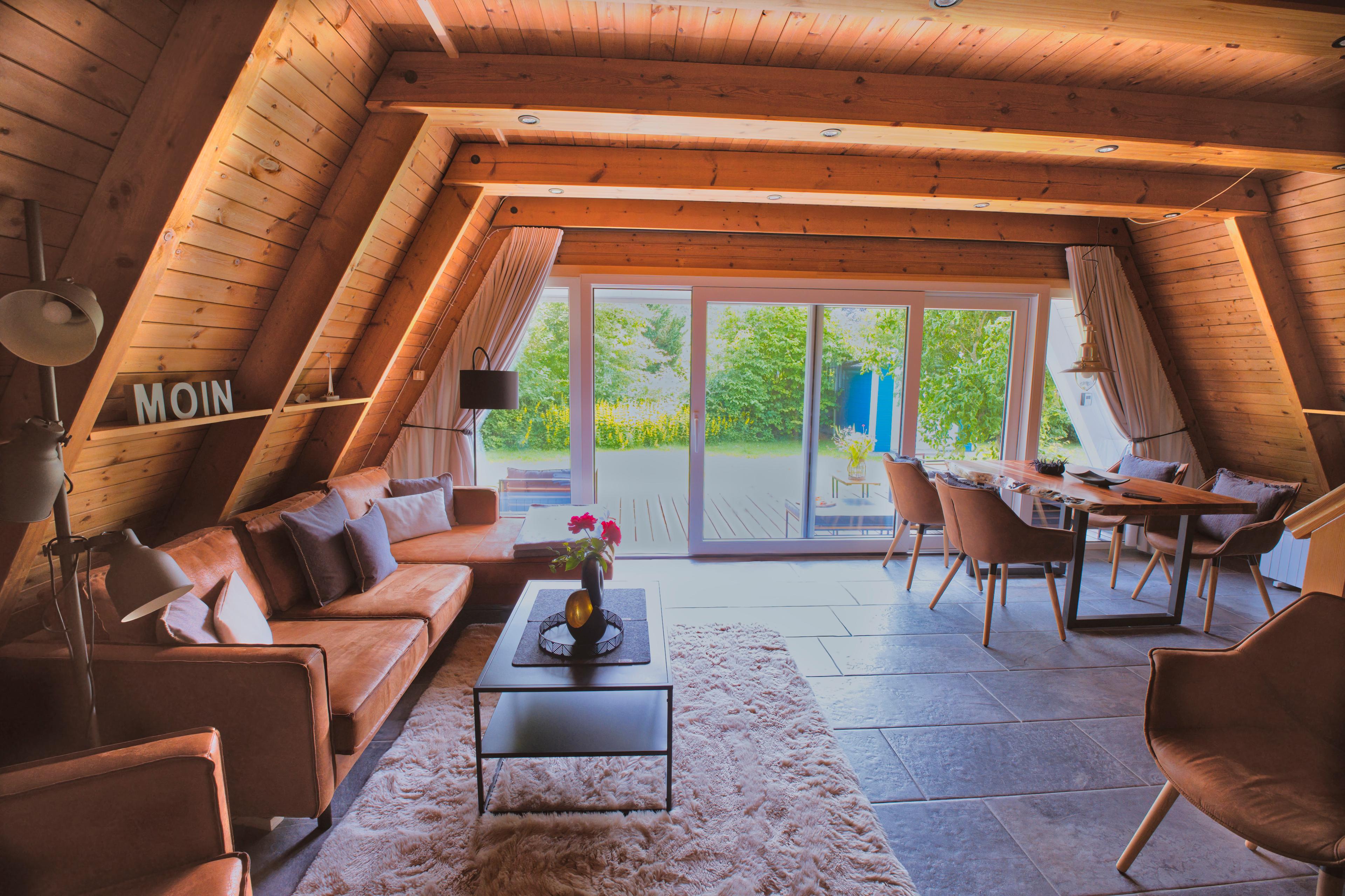 Ein gemütliches Wohnzimmer mit Holzwänden, braunen Ledersofas, einem flauschigen Teppich und einem großen Panoramafenster mit Blick auf einen Garten.