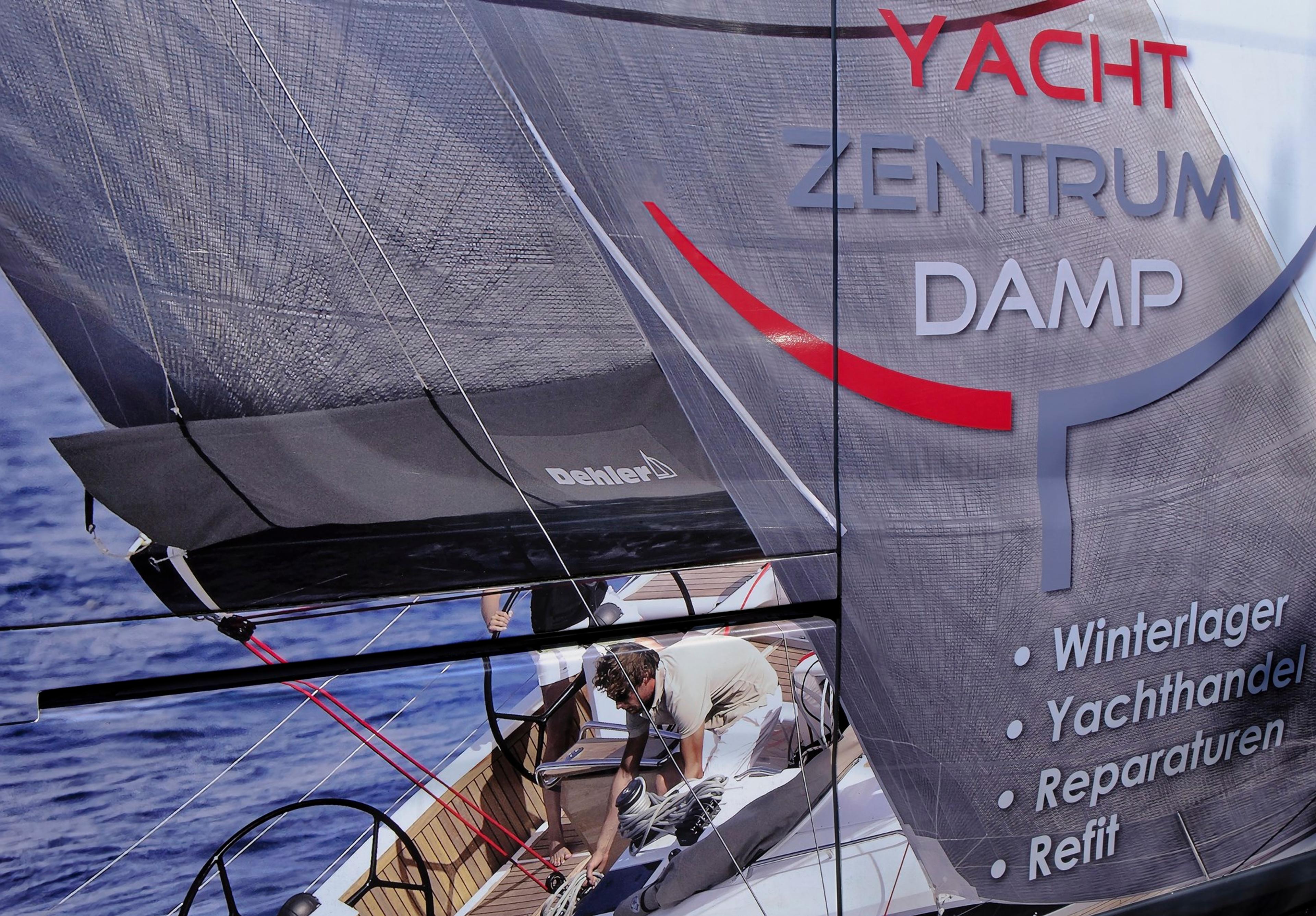 Werbung für Yacht Zentrum Damp auf einem Segelboot mit Personen an Bord