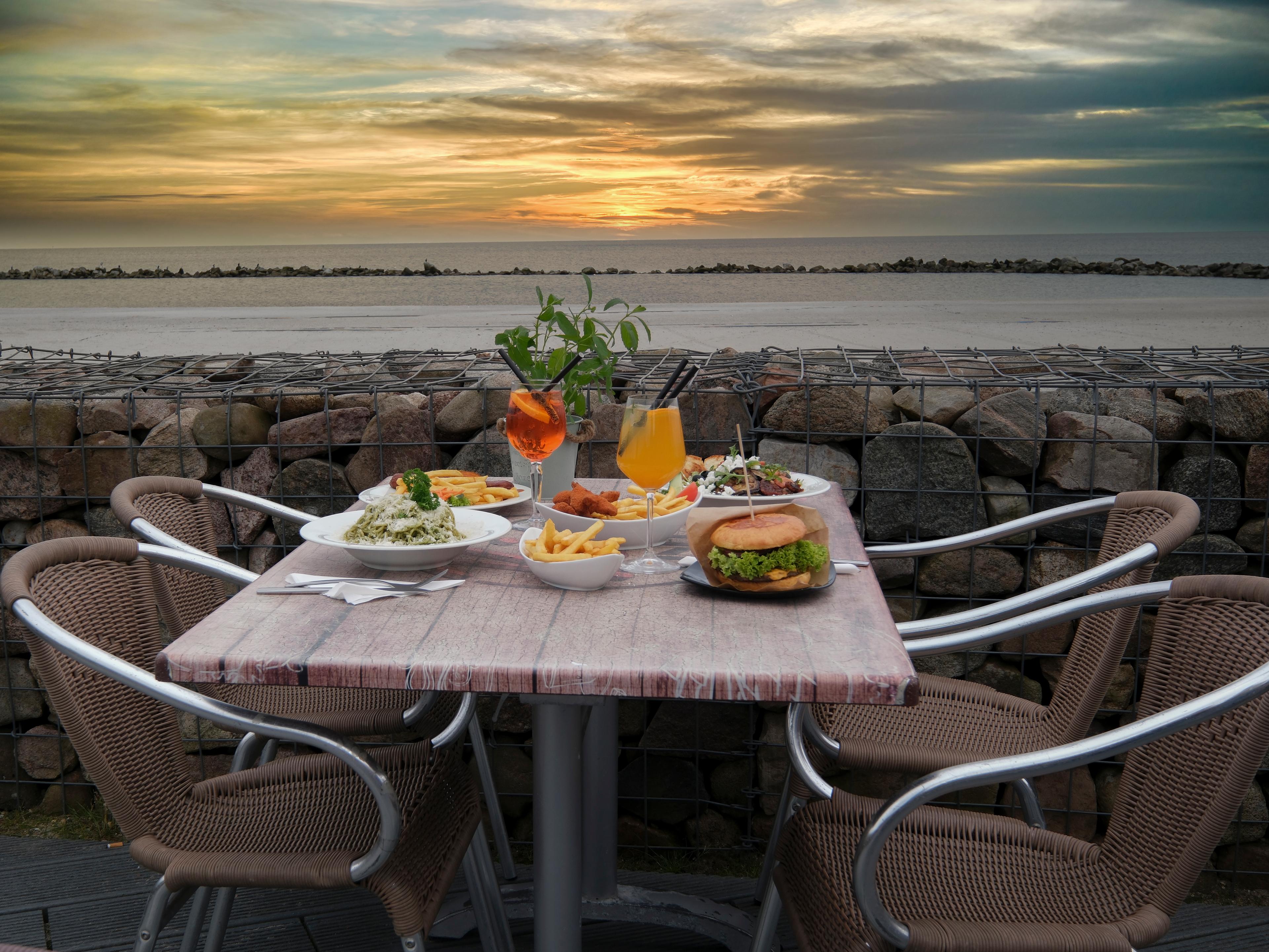 Ein Tisch in einem Strandrestaurant mit verschiedenen Gerichten und Getränken bei Sonnenuntergang