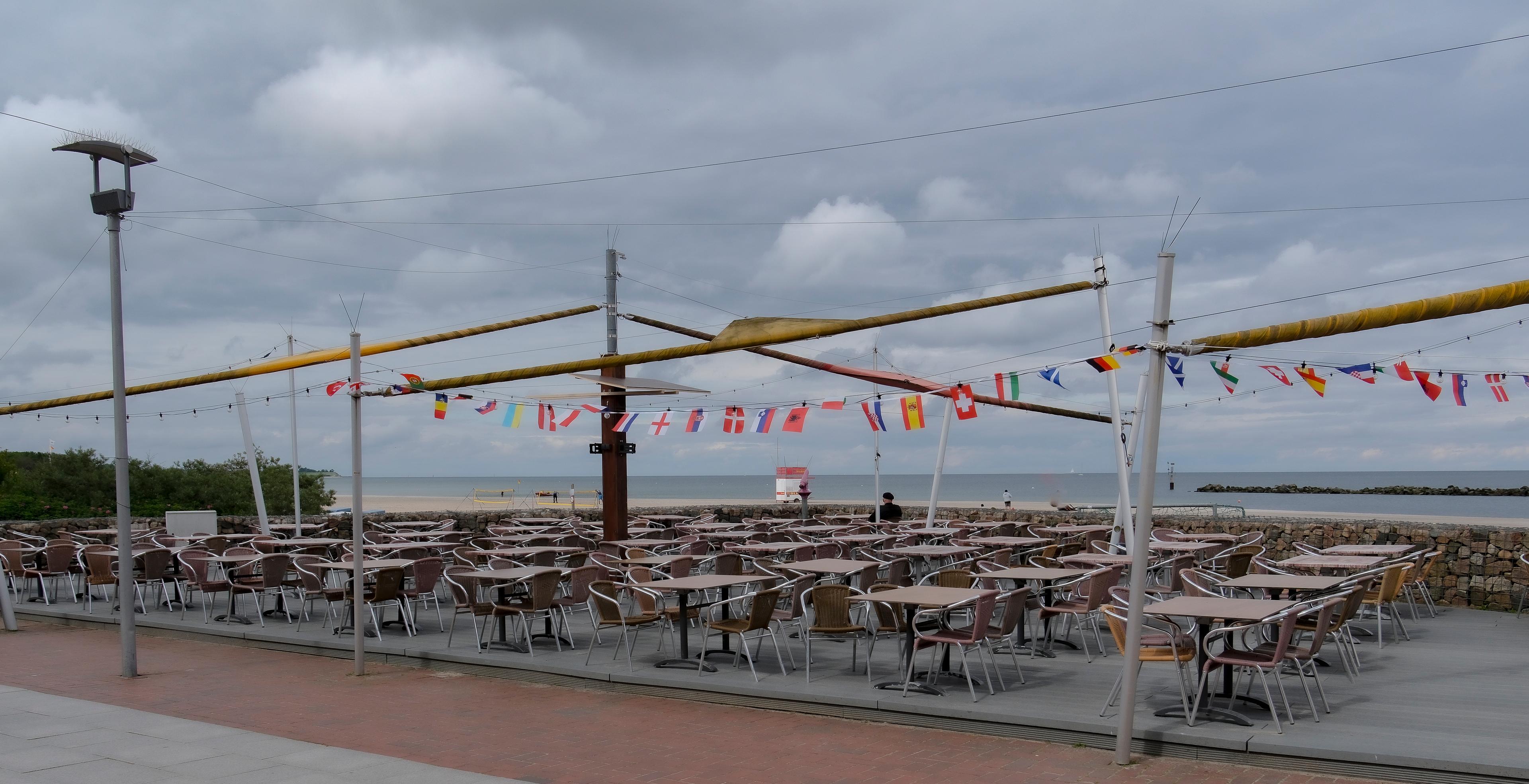 Ein leeres Strandcafé mit Tischen und Stühlen, dekoriert mit internationalen Flaggen, mit Blick auf das Meer