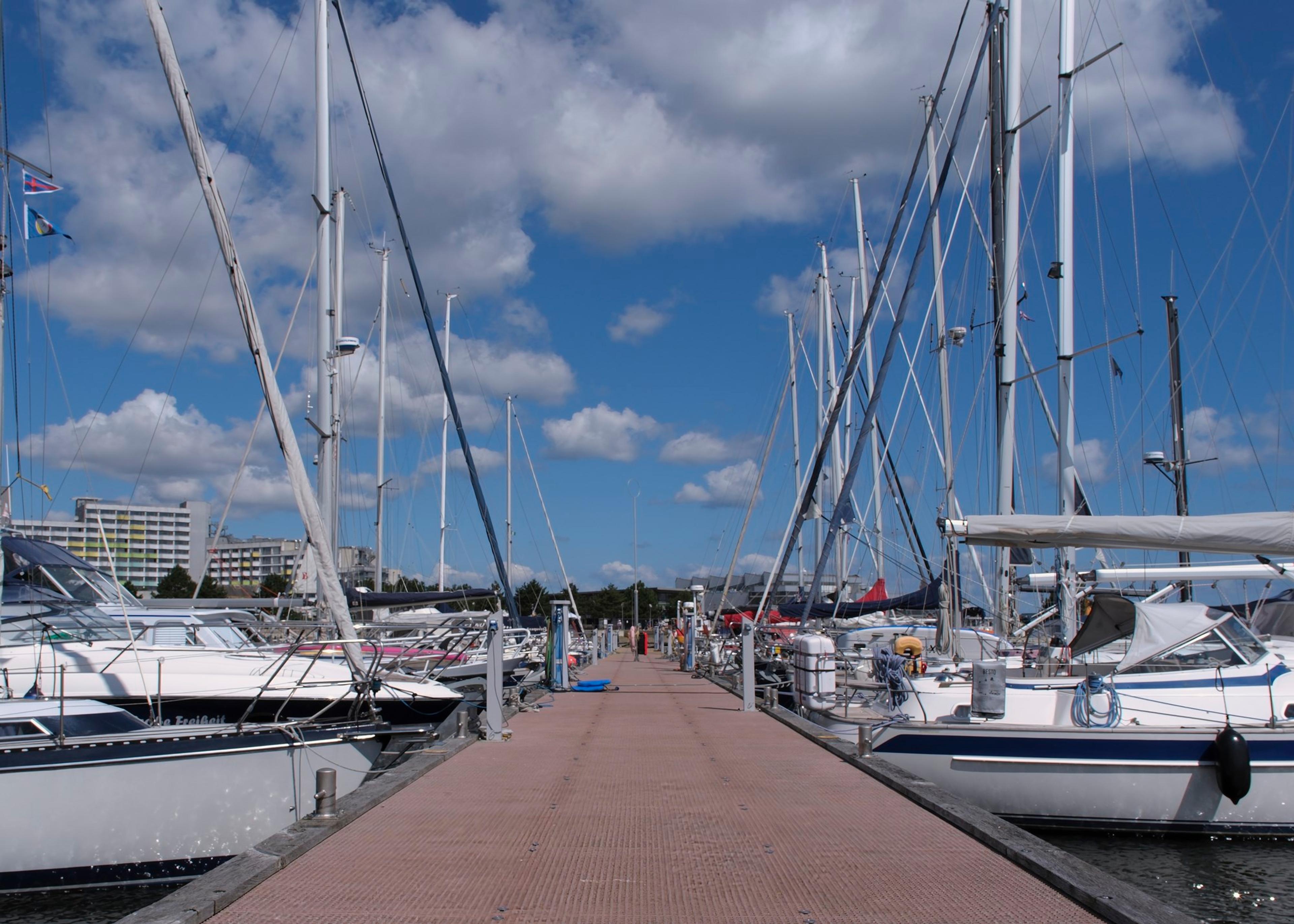 Ein Yachthafen mit mehreren Segelbooten, die an einem Steg festgemacht sind, unter einem klaren blauen Himmel mit weißen Wolken.