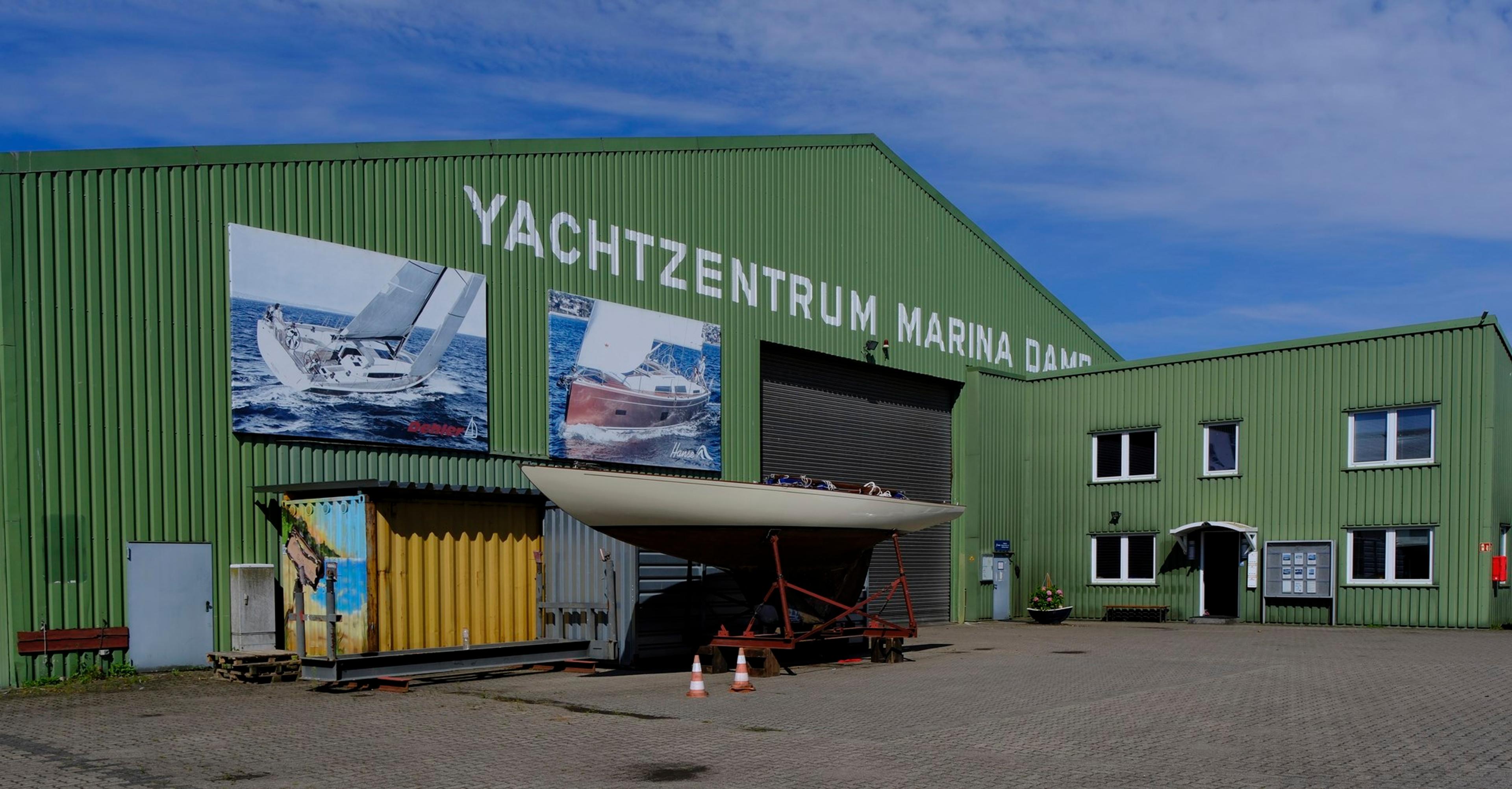 Grünes Gebäude des Yachtzentrums Marina Damp mit einem Boot auf einem Anhänger