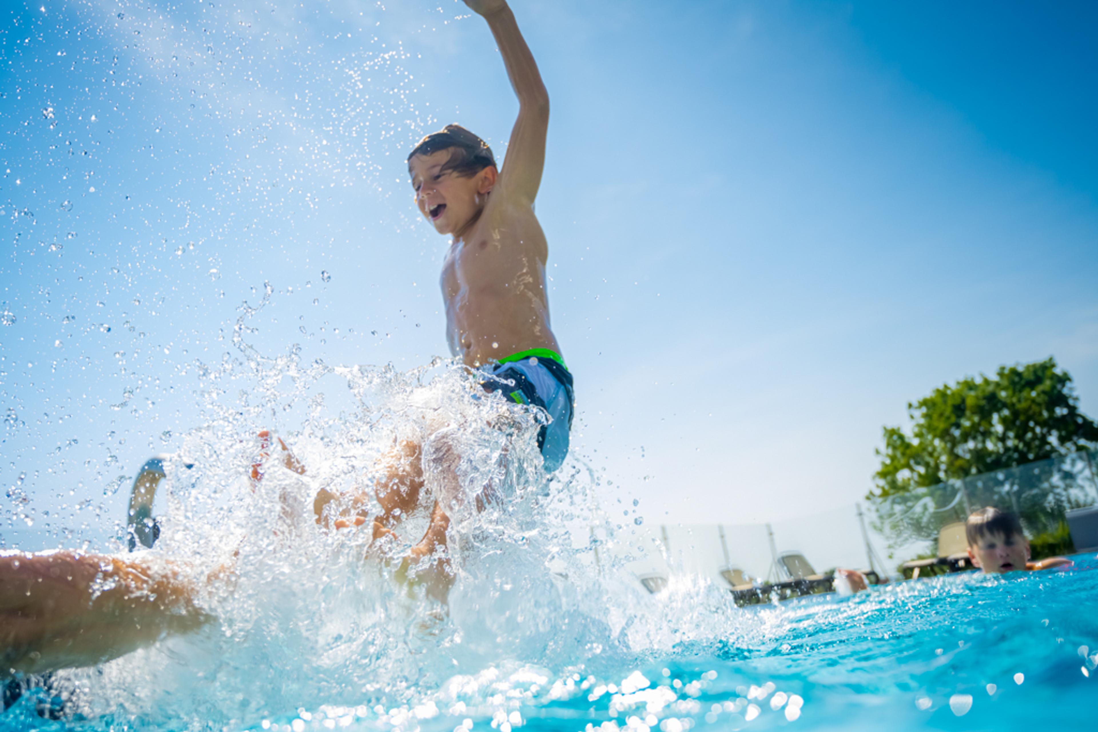 Ein Junge in Badehose springt mit Freude ins Schwimmbad, während Wasser spritzt