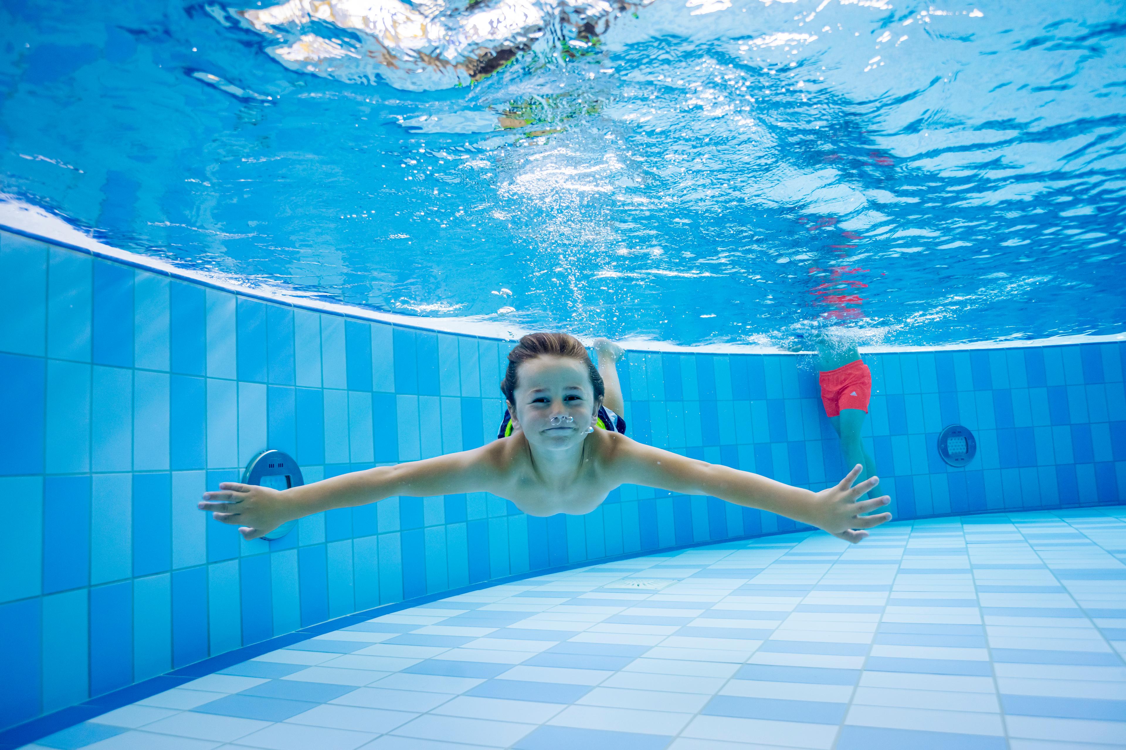 Ein Kind schwimmt unter Wasser in einem gefliesten Pool mit ausgestreckten Armen