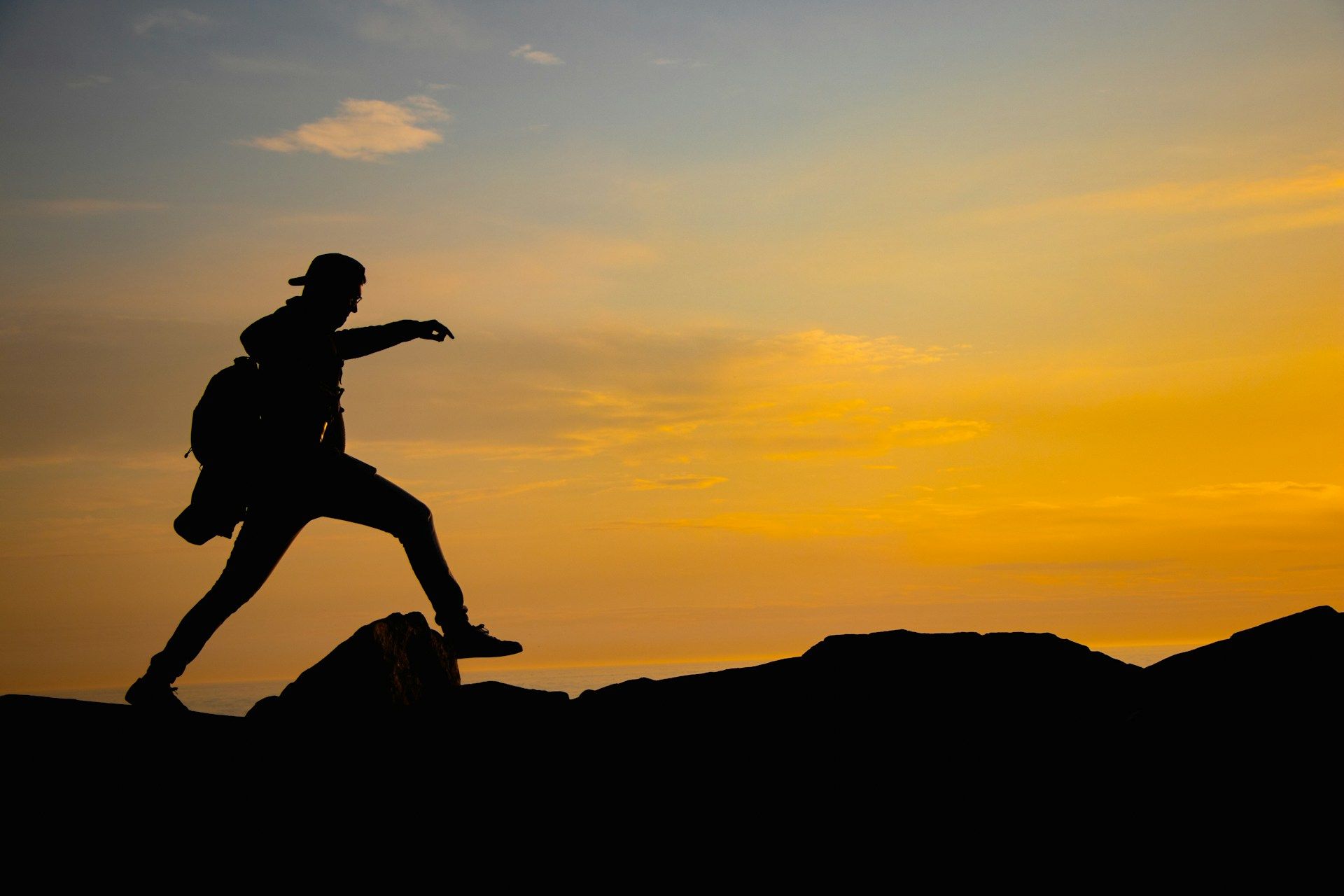 Silhouette of a hiker stepping across rocks during sunset