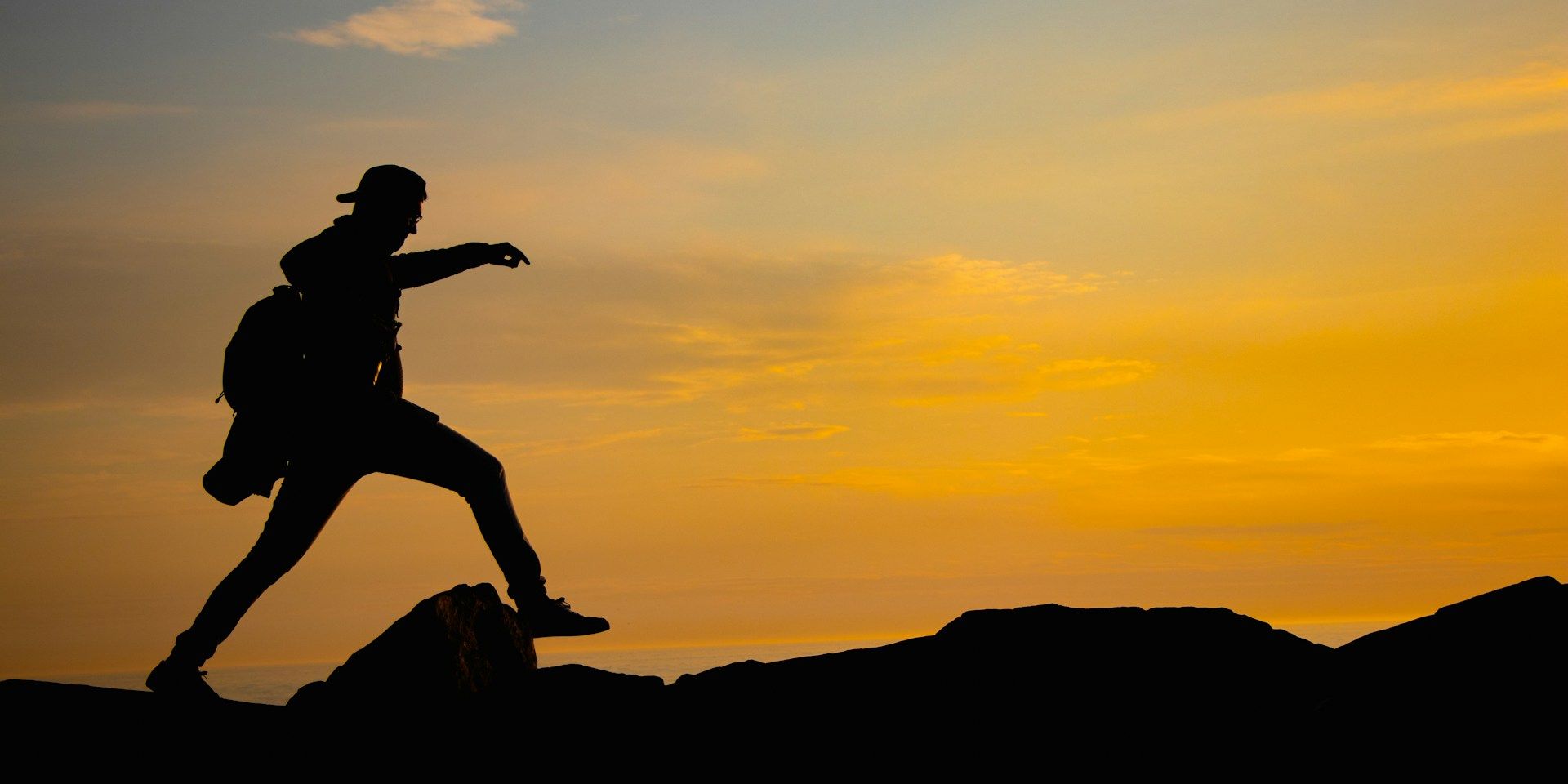 Silhouette of a hiker stepping across rocks during sunset