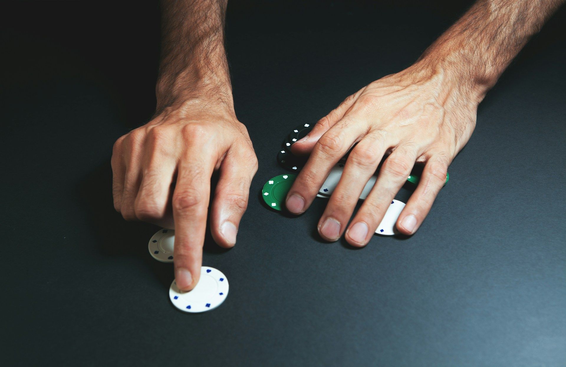 Hands arranging poker chips on a black table, close-up view of a card game in progress.