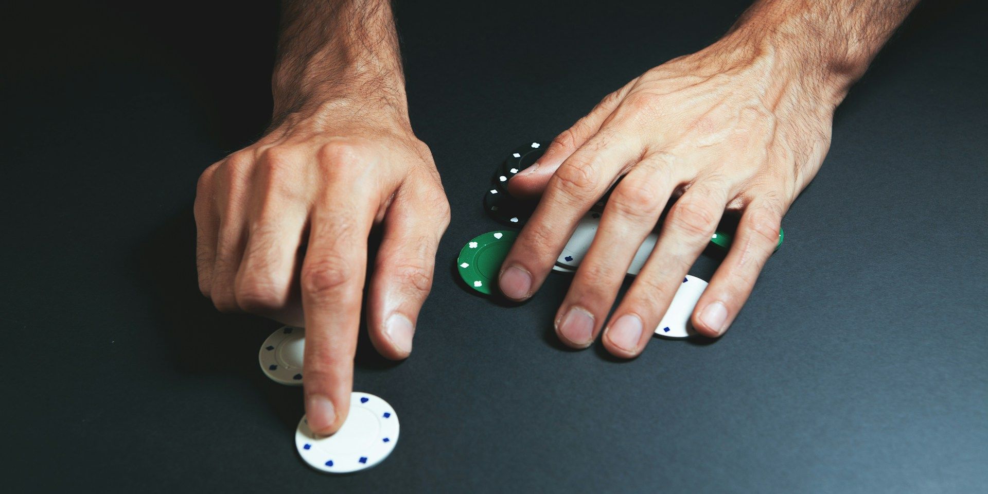 Hands arranging poker chips on a black table, close-up view of a card game in progress.