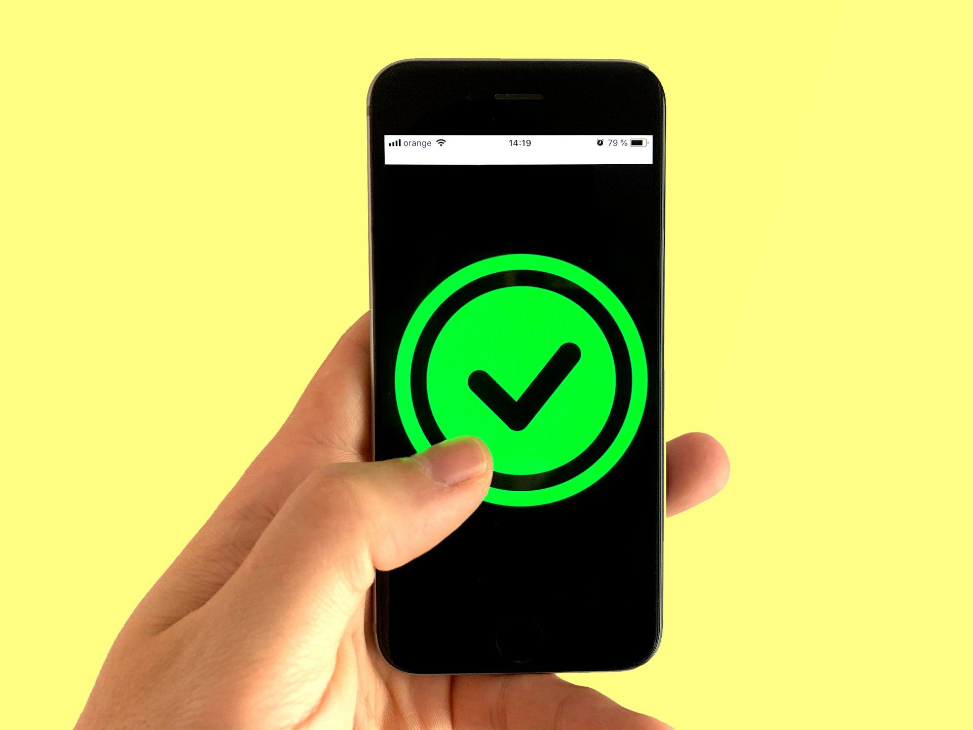 Hand holding smartphone showing a green checkmark on screen against a yellow background
