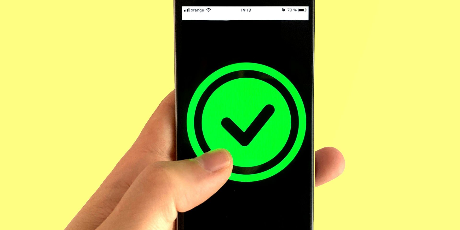 Hand holding smartphone showing a green checkmark on screen against a yellow background