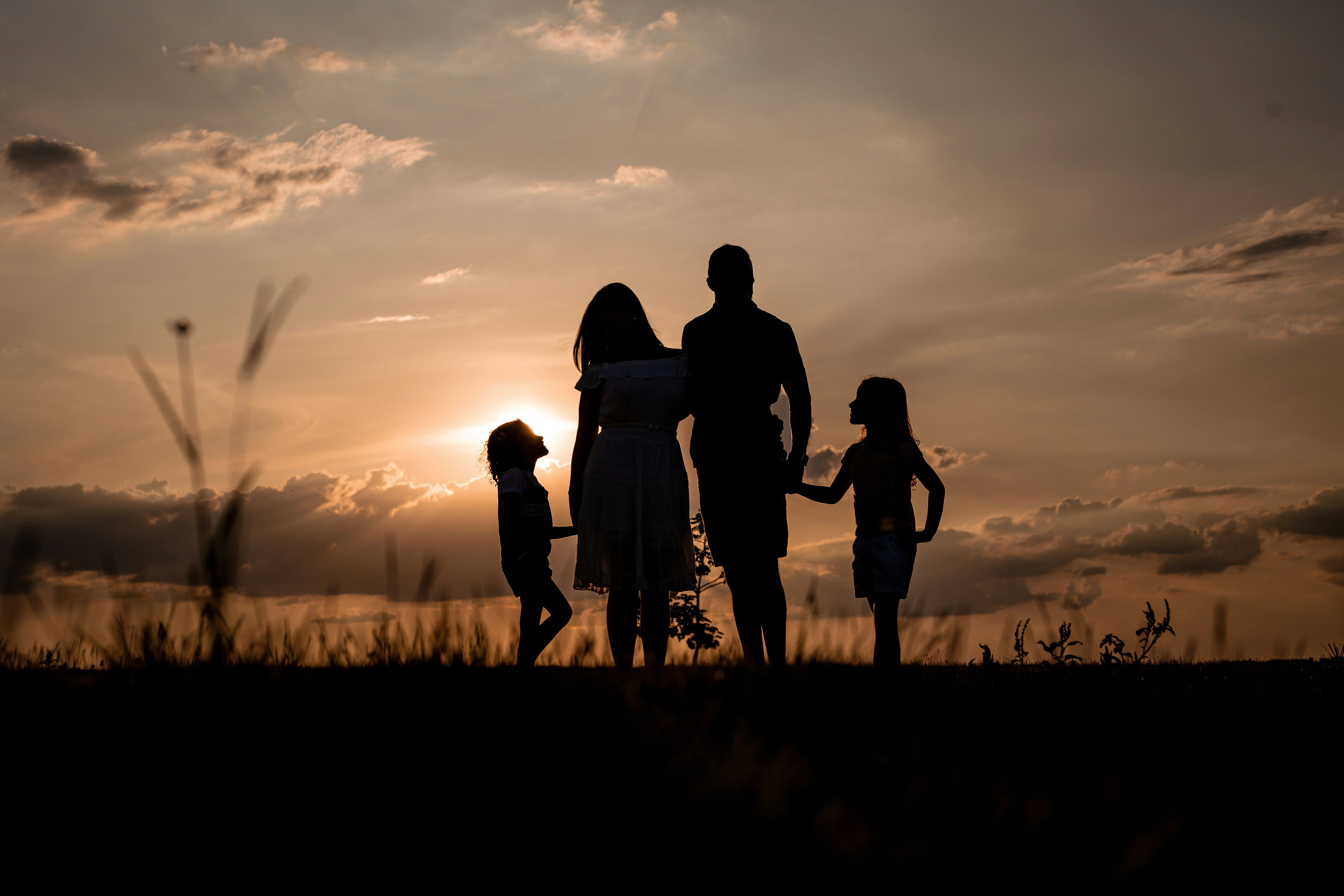 Family of four standing outdoors at sunset, holding hands.