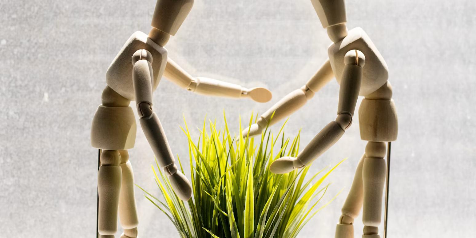 two wooden mannequins leaning over a potted plant